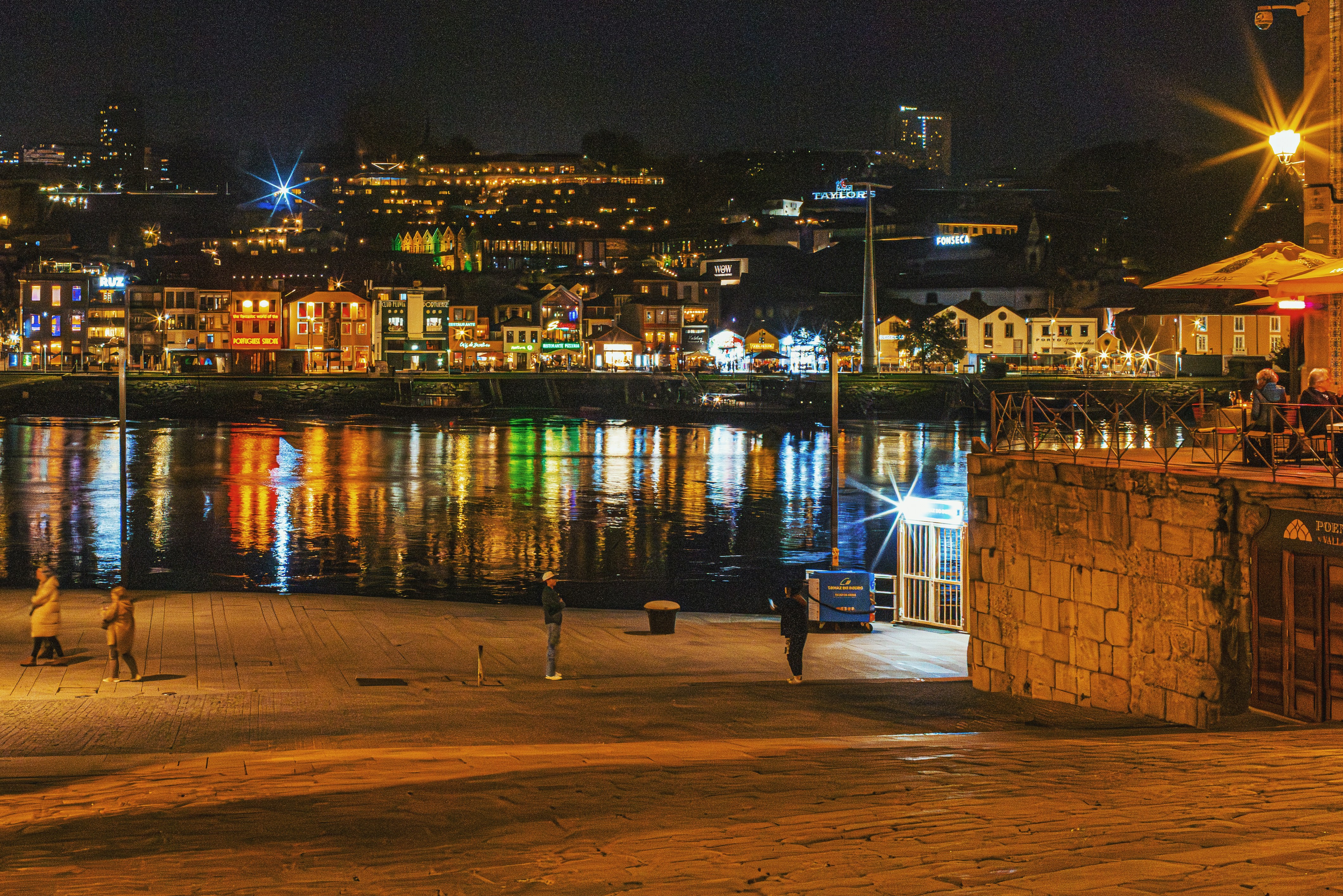 Stadtbild mit beleuchteten Gebäuden, die nachts im Wasser reflektieren.