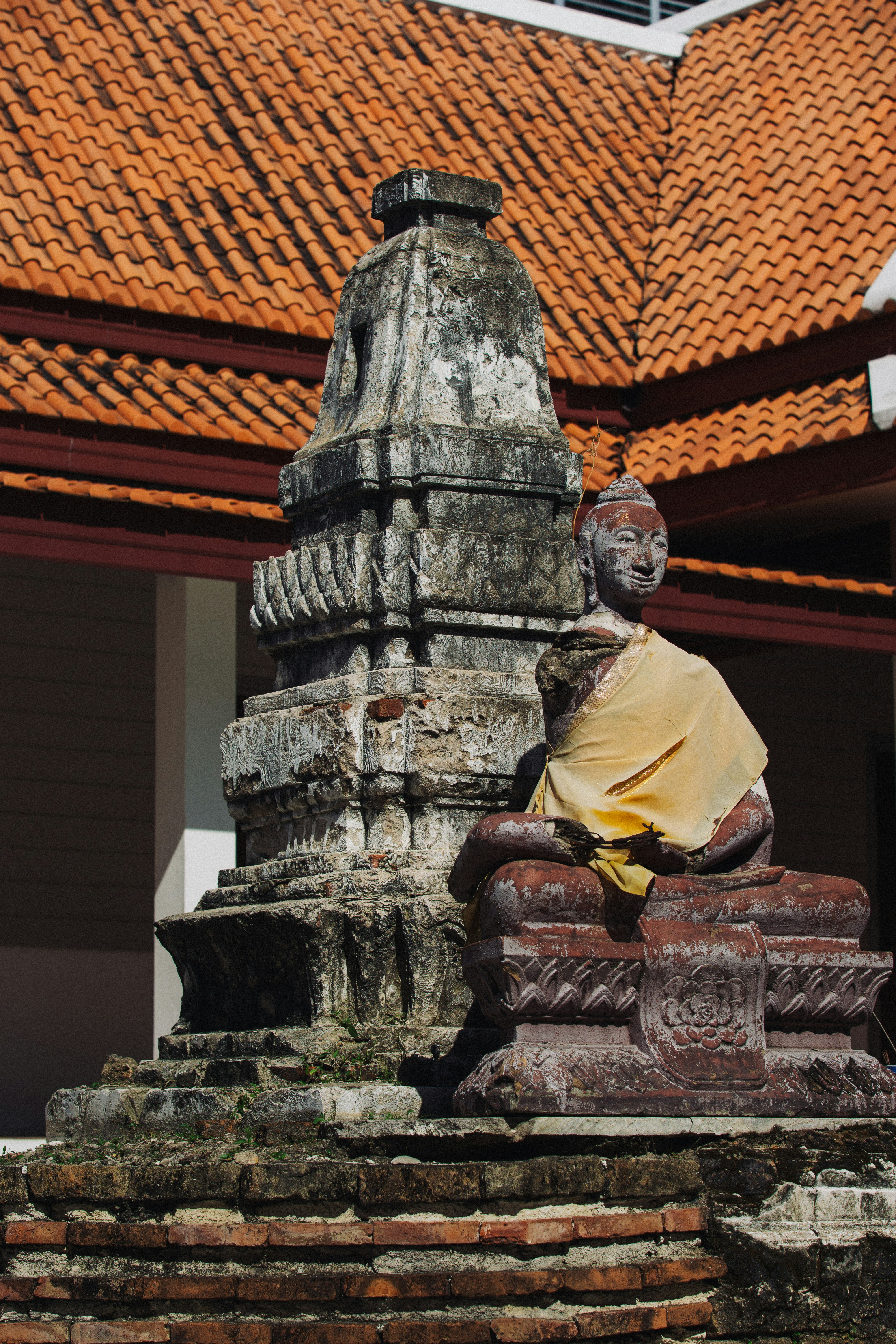 Weathered buddha statue with yellow cloth and stupa