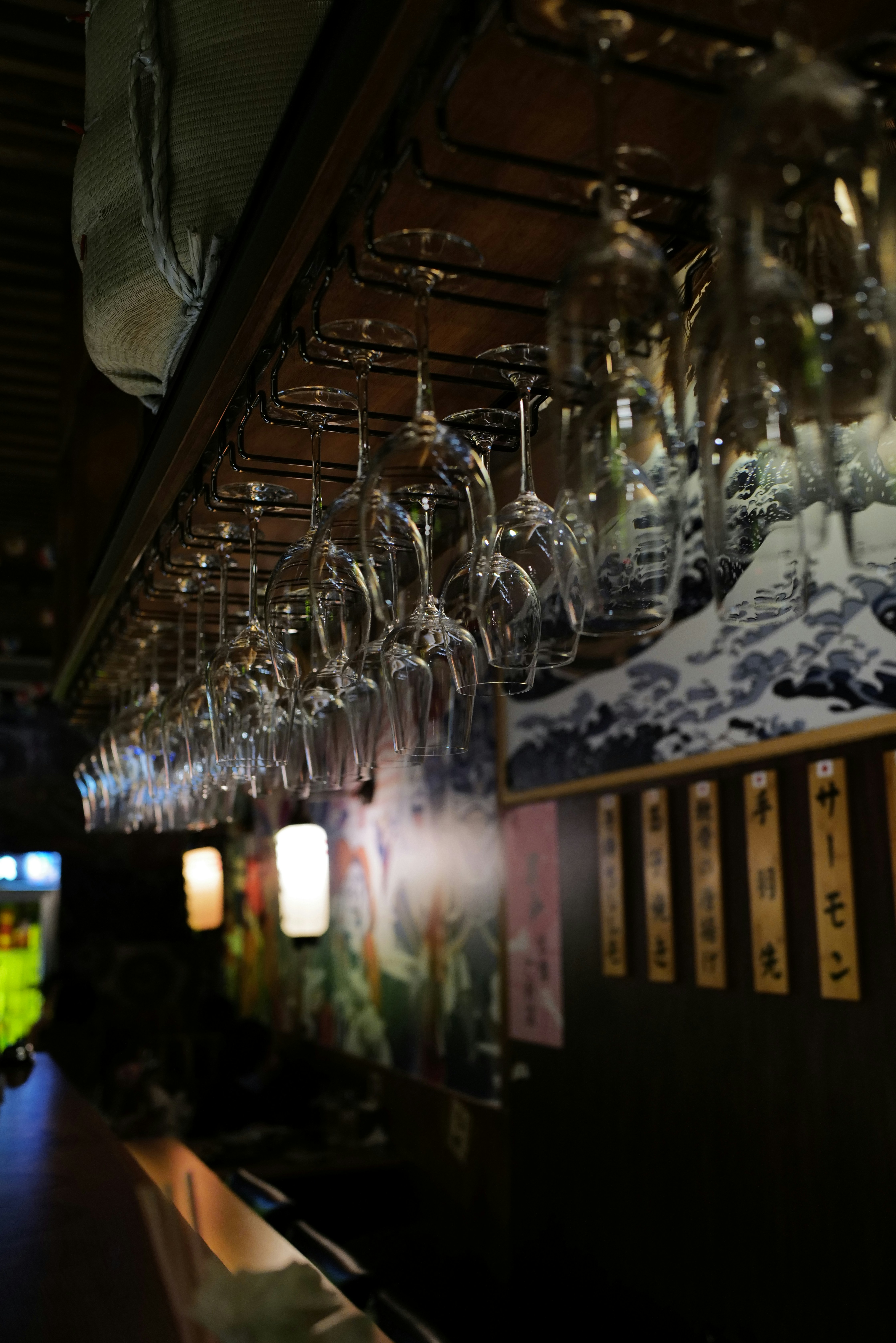 Copas de vino cuelgan sobre una barra con arte japonés.