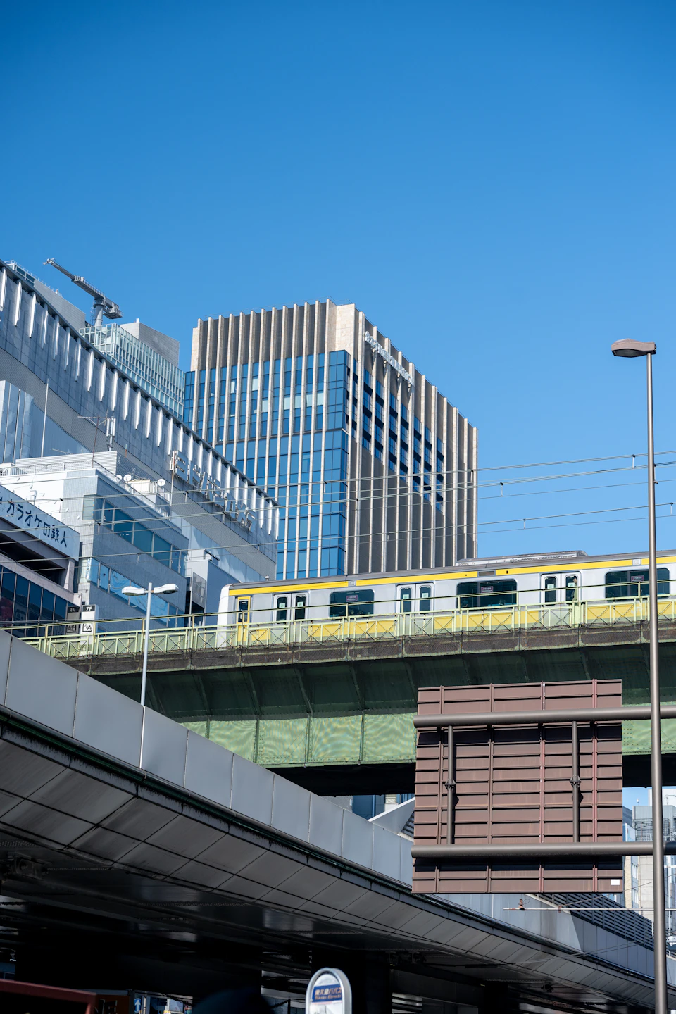 Vibrant yellow and green train crosses elevated railway track in bustling city scene