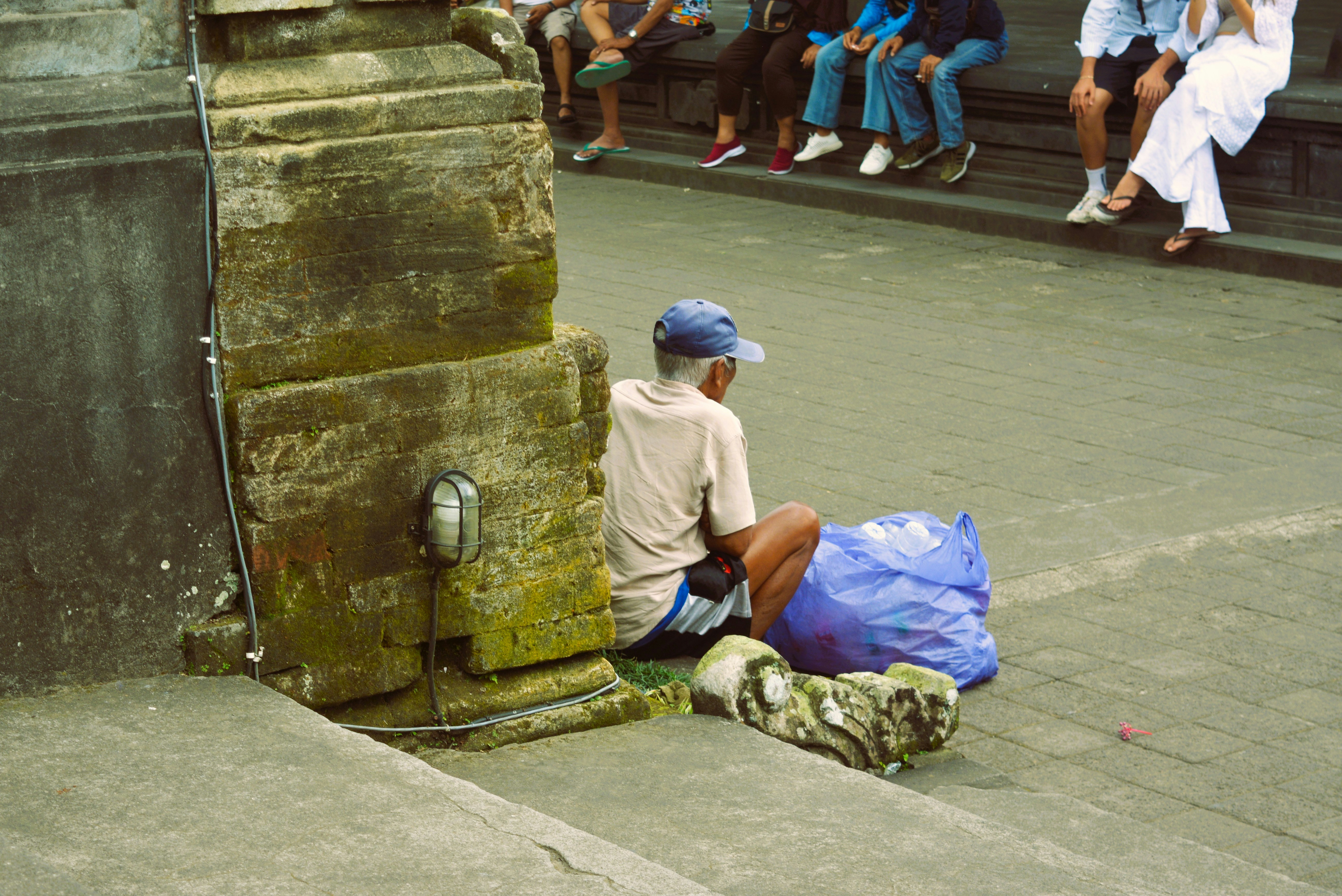 Man sitting by ancient stone structure with blue bag
