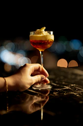 A hand holding a cocktail with foamy topping