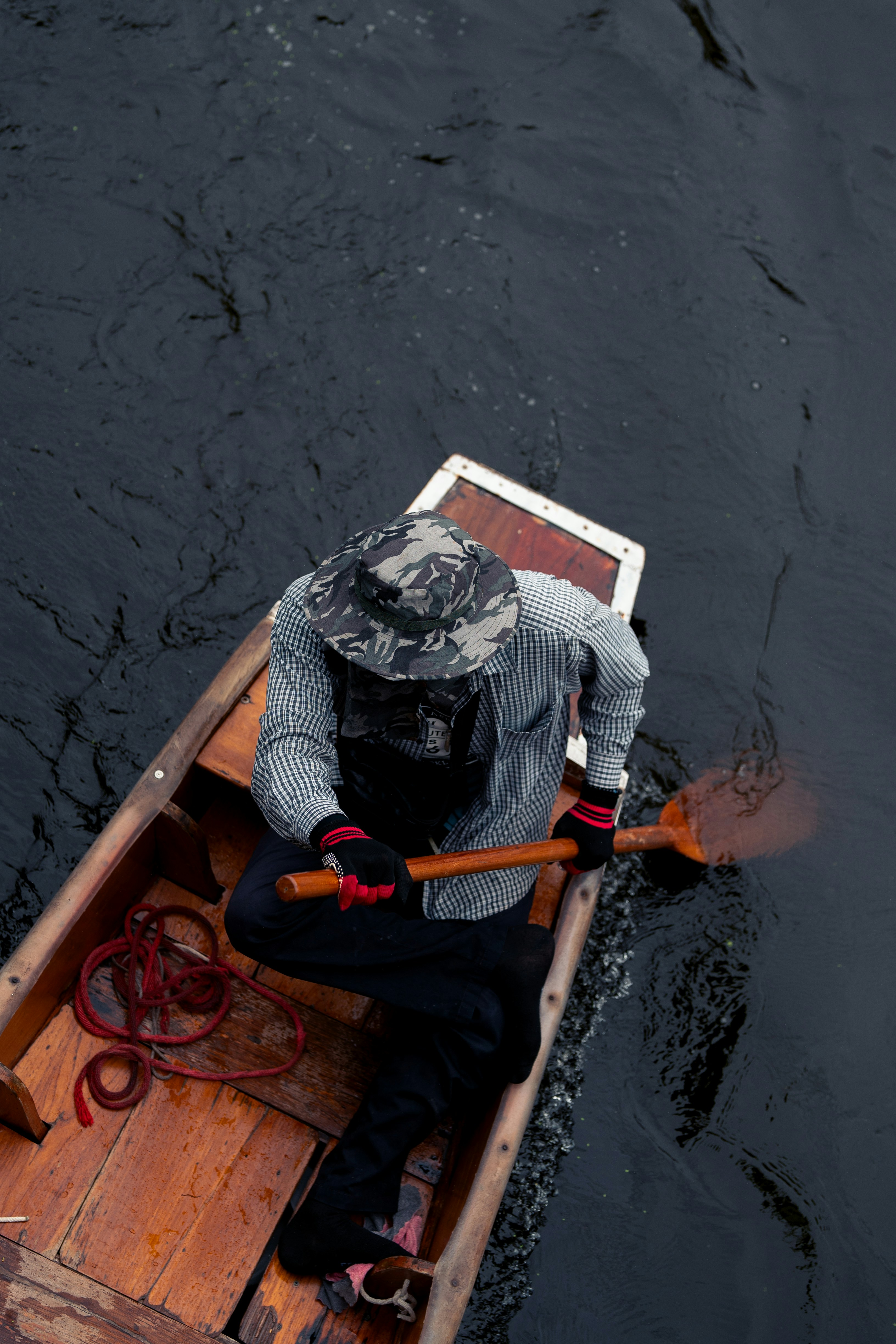 모자를 쓴 남자가 어두운 물 위에서 나무 배를 젓고 있다
