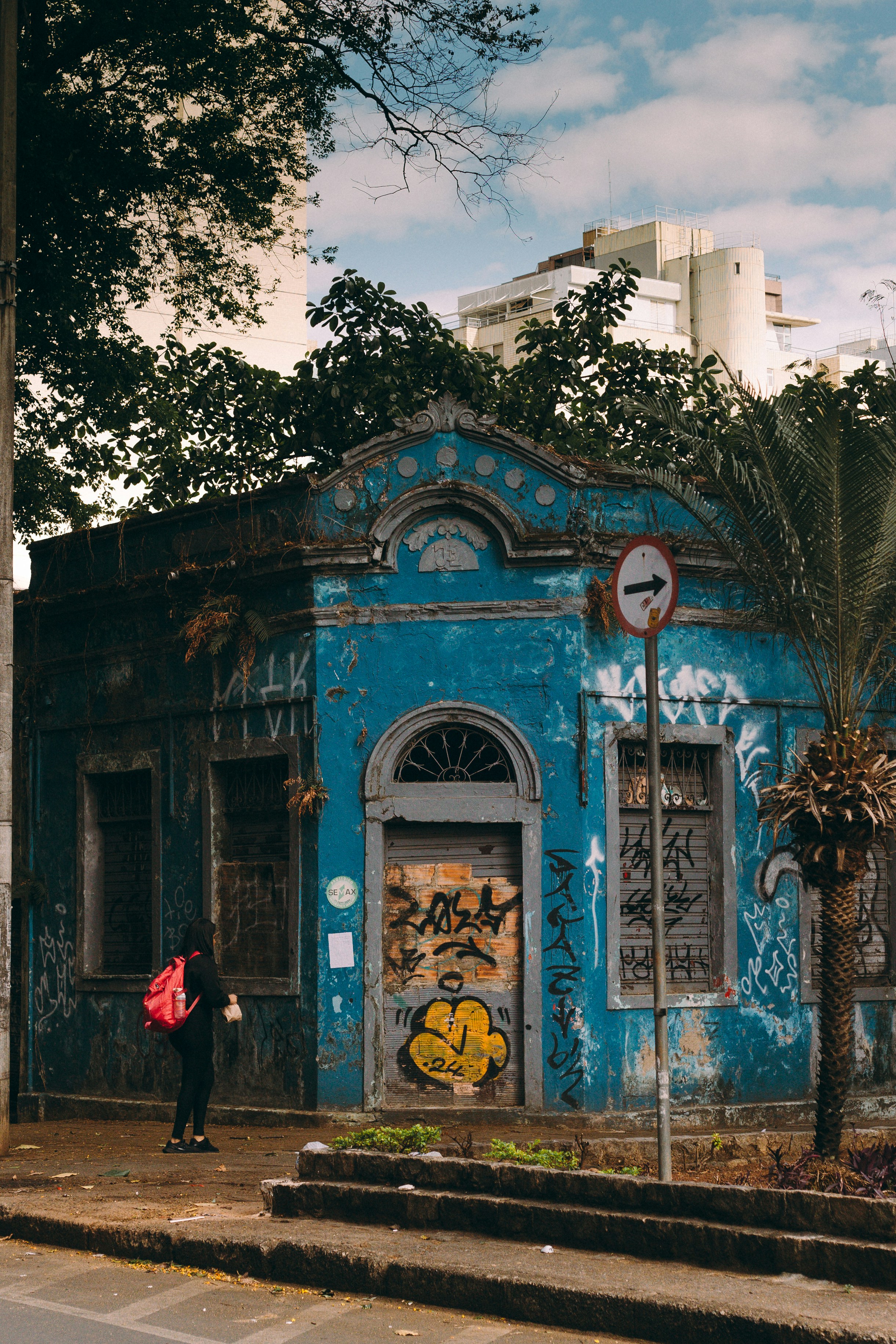 A person stands outside a blue, graffiti-covered building.