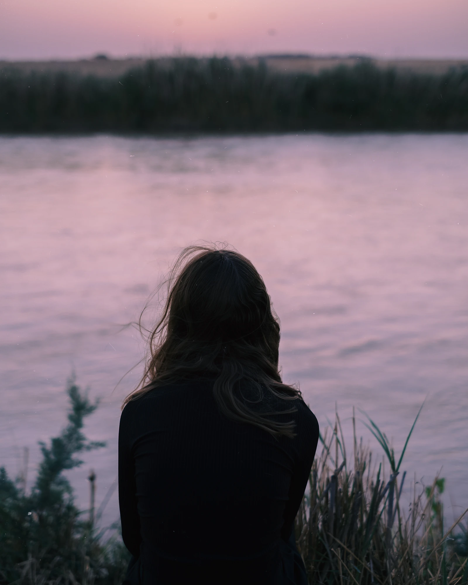 A woman sitting quietly by a calm lake at dusk, representing the nervous system settling in the evening with fibromyalgia