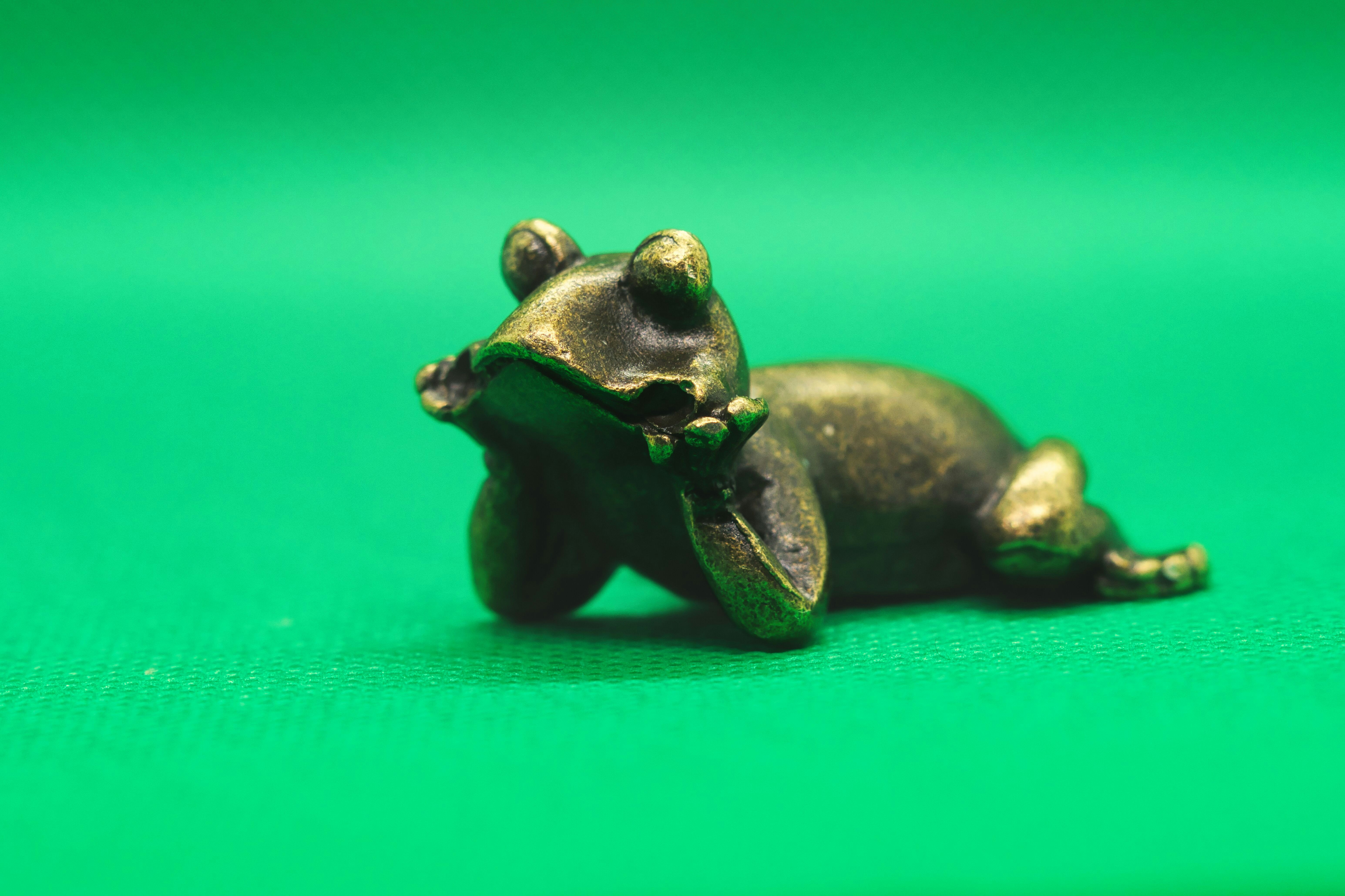 Une petite statue de grenouille en bronze repose sur une surface verte