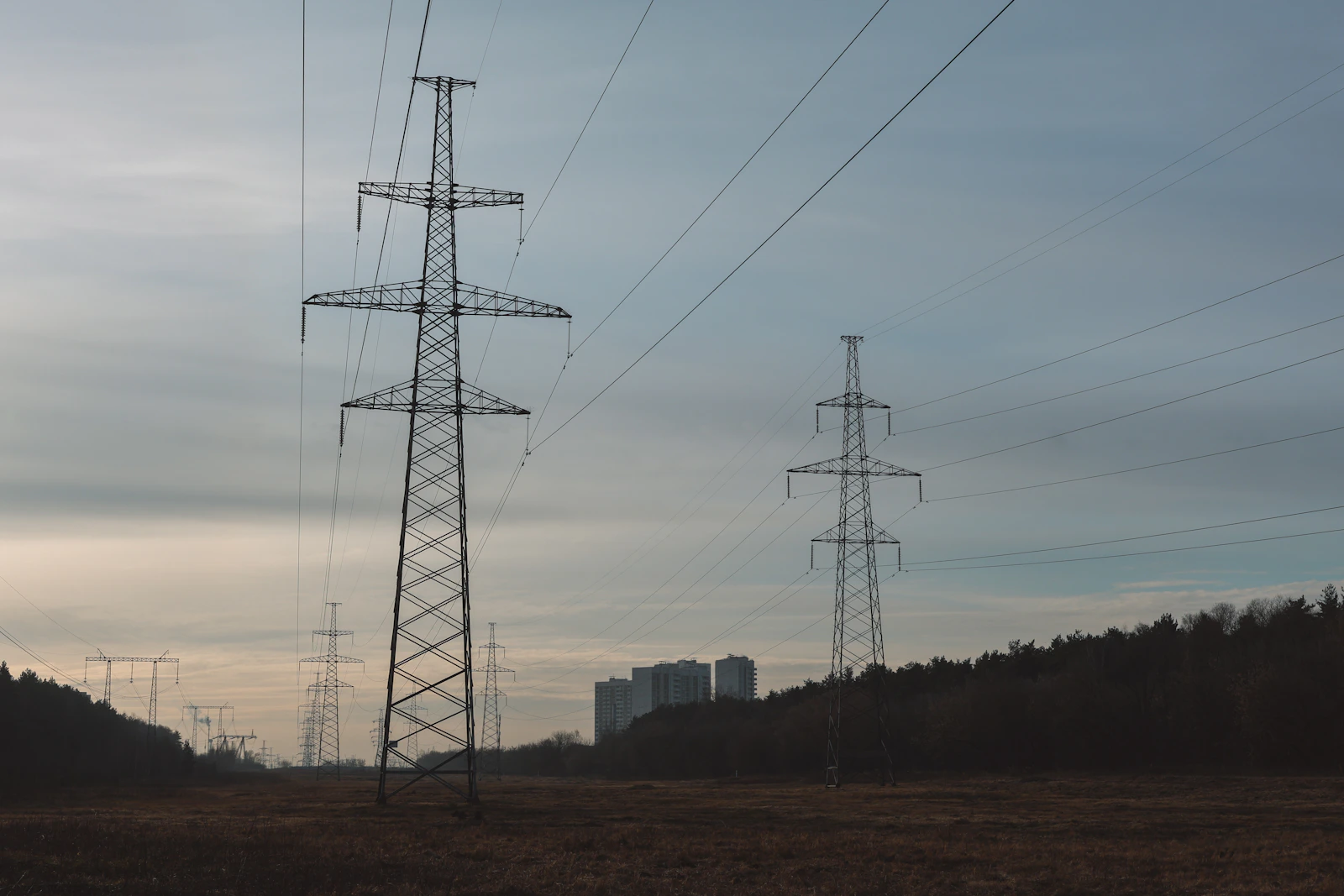 Power lines stretch across a field towards distant buildings