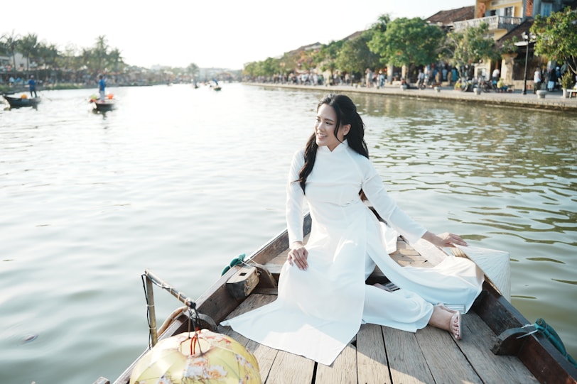 Vietnam’s National Dress: The Elegance of the Ao Dai Woman in white Ao Dai dress on boat by a river.
