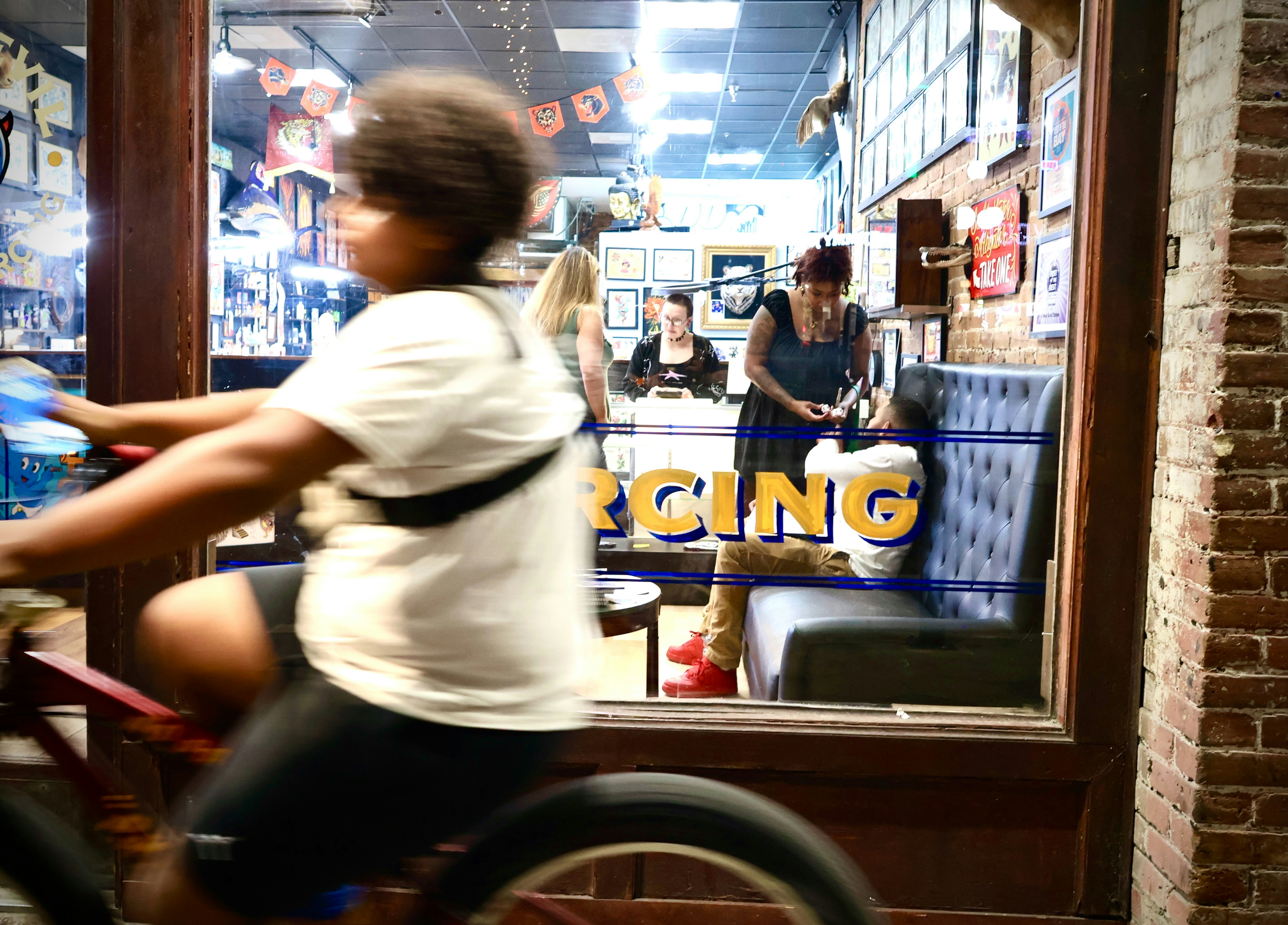 Person rides bicycle past piercing studio window