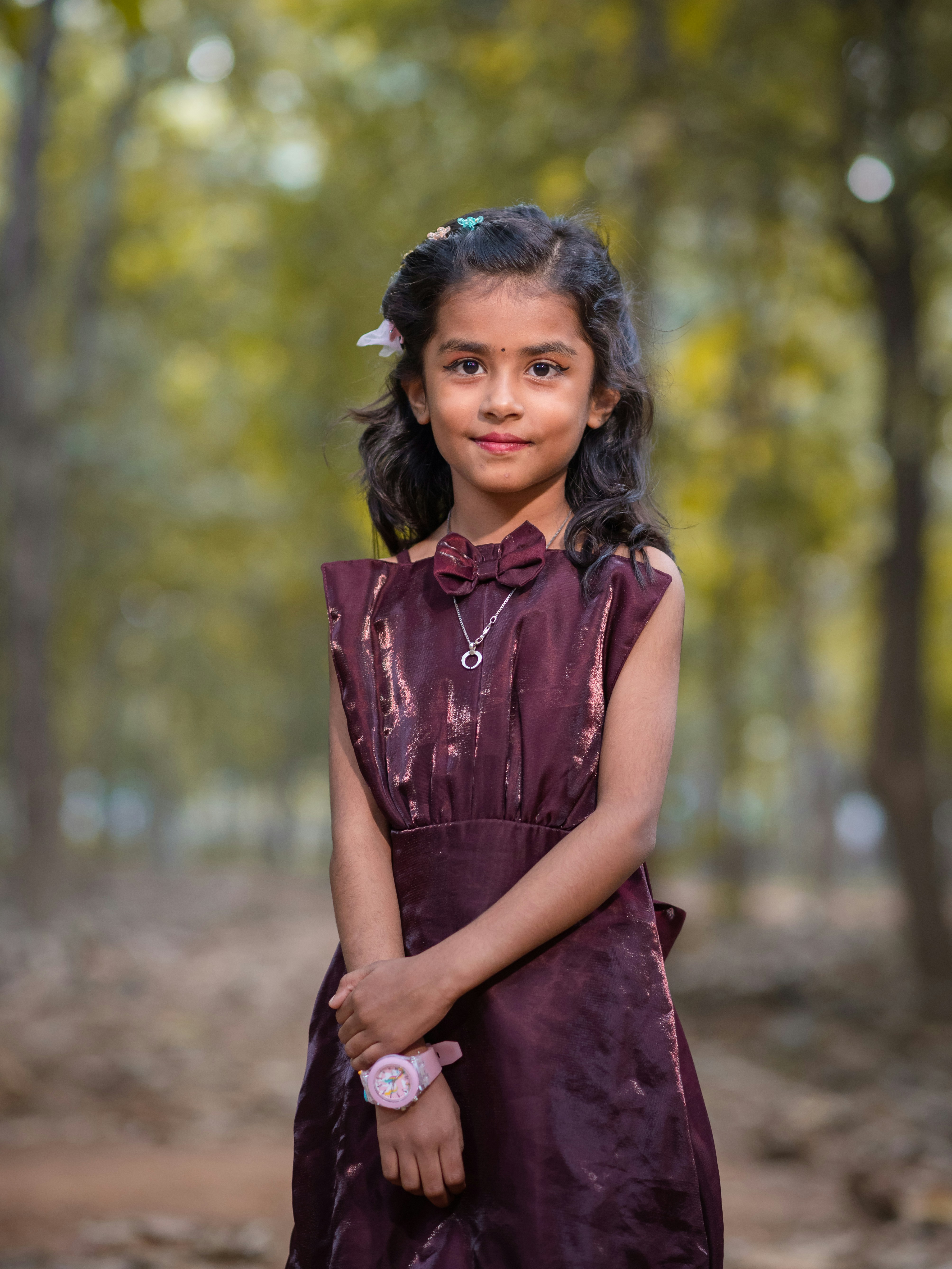 Young girl in a maroon dress stands in a forest.