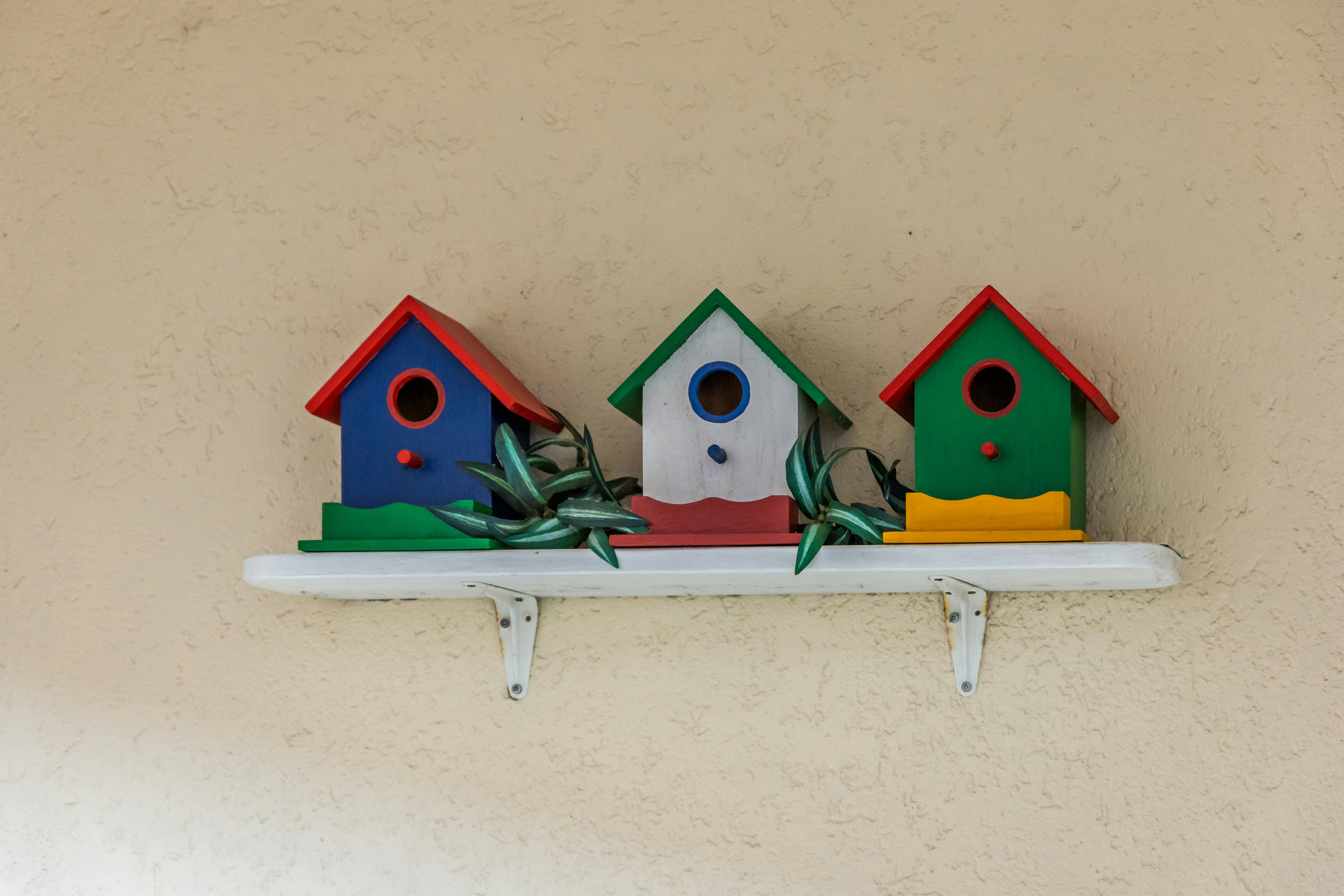 Three colorful birdhouses on a white shelf.