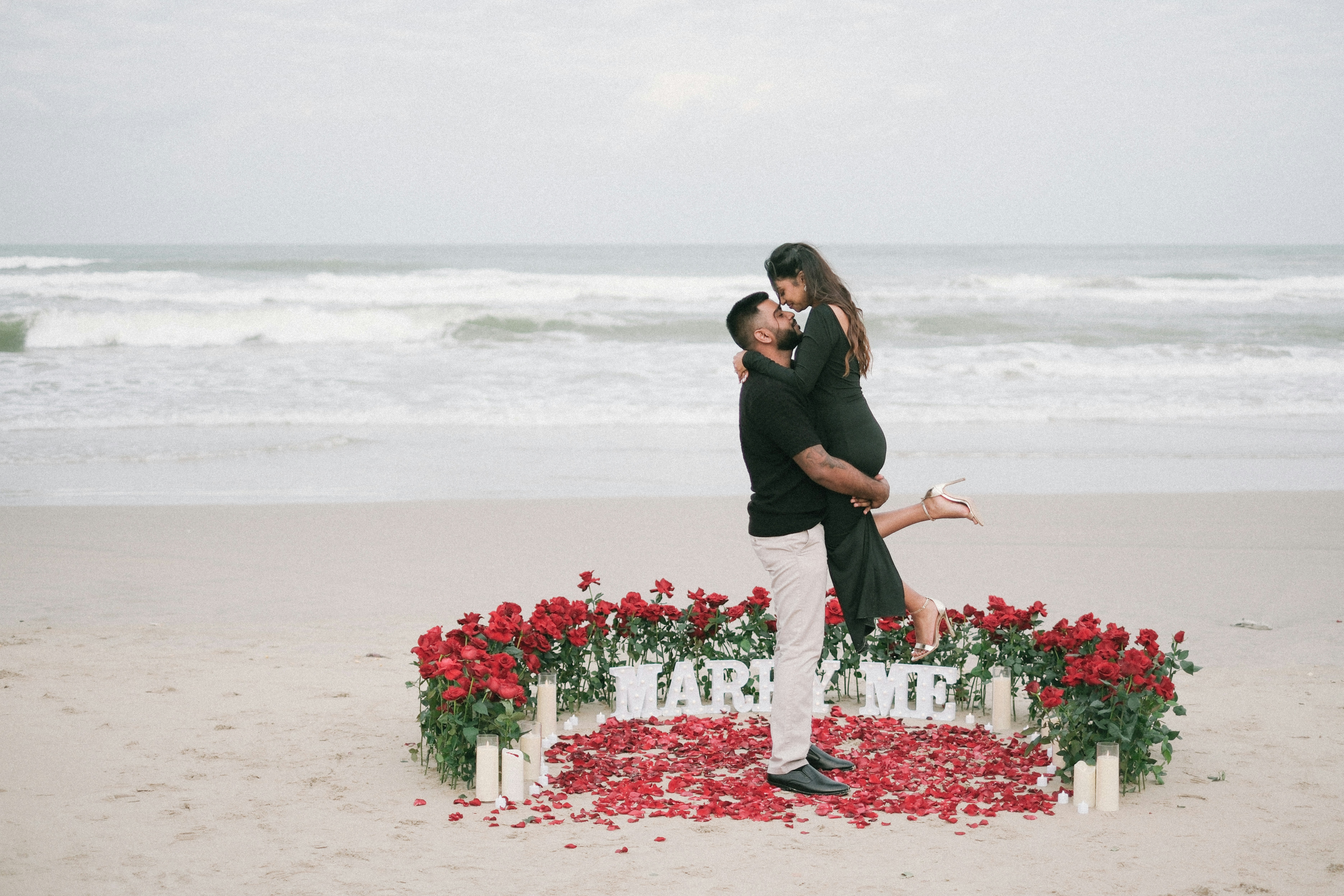 Man proposes to woman on beach with roses.