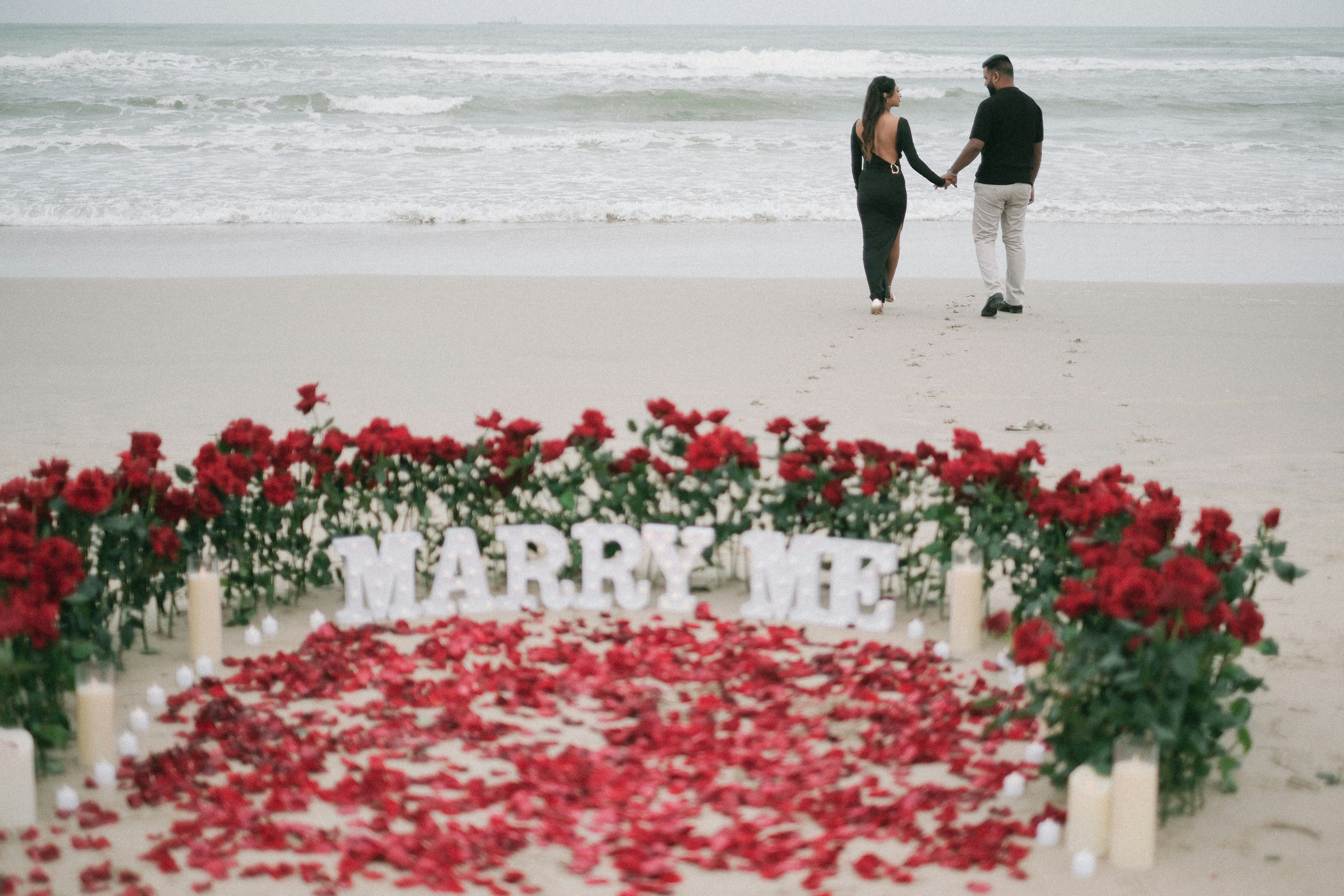 Couple walking on beach with rose petal proposal