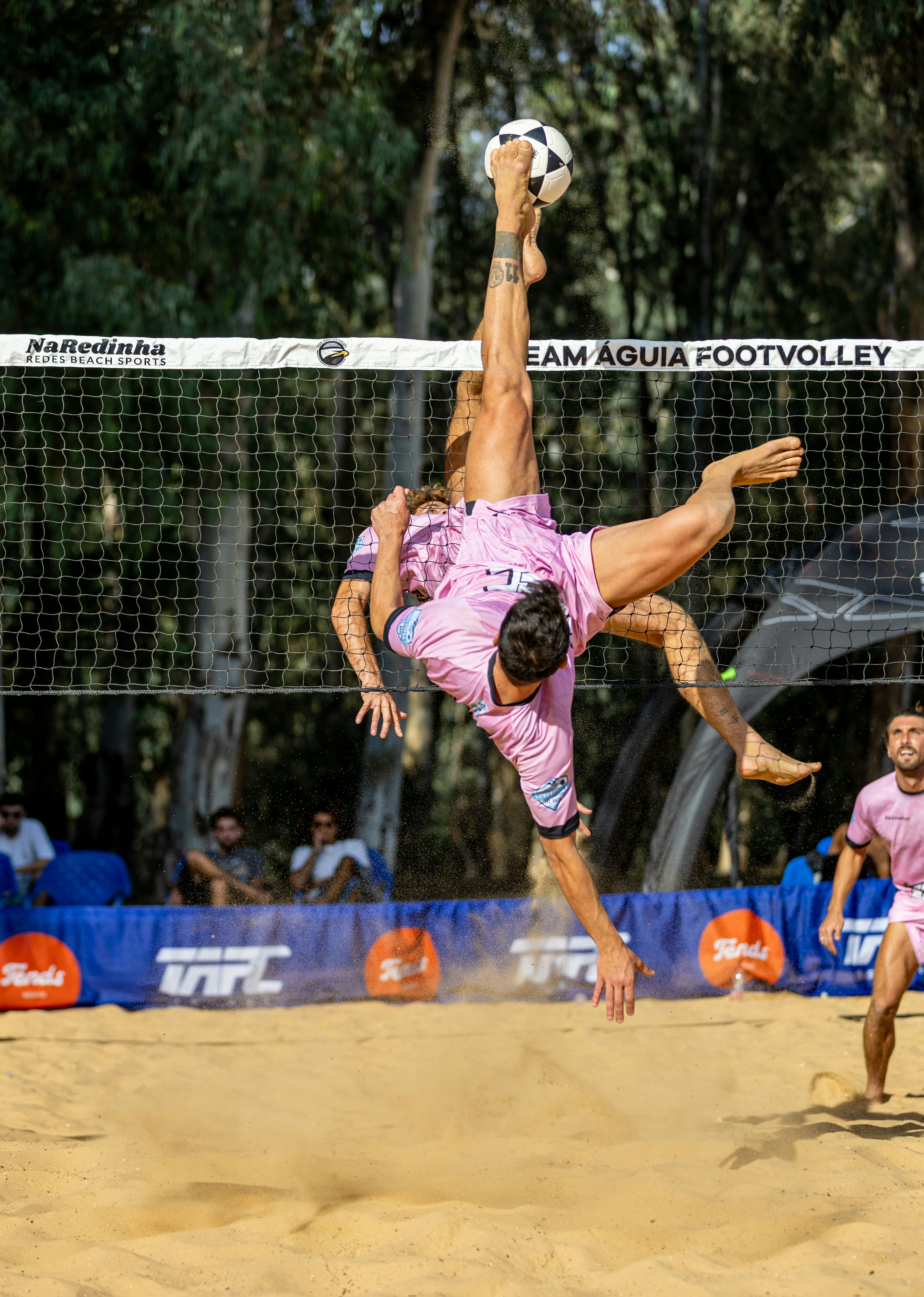Man performs acrobatic kick with soccer ball over net.