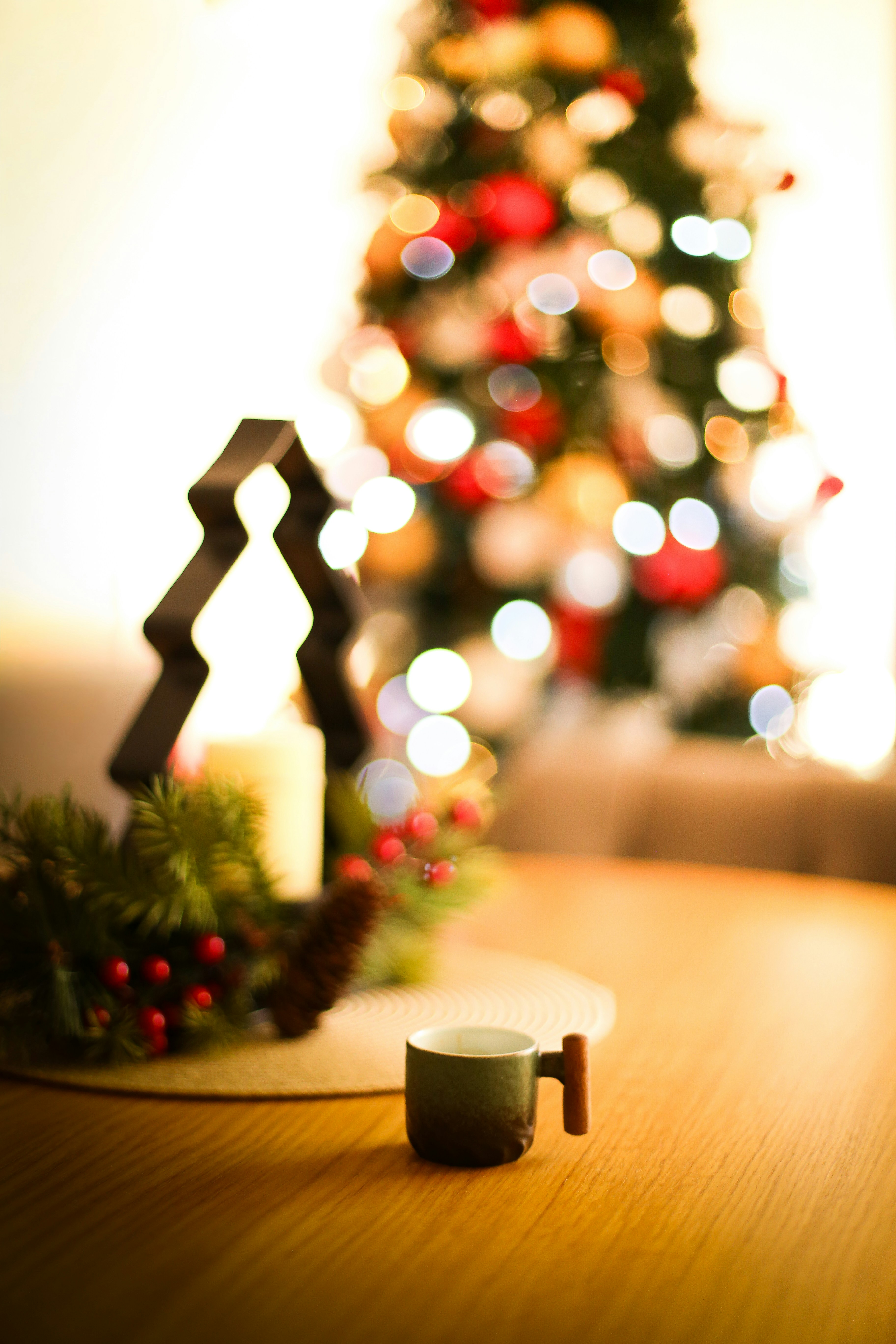 A small mug on a table with a christmas tree.