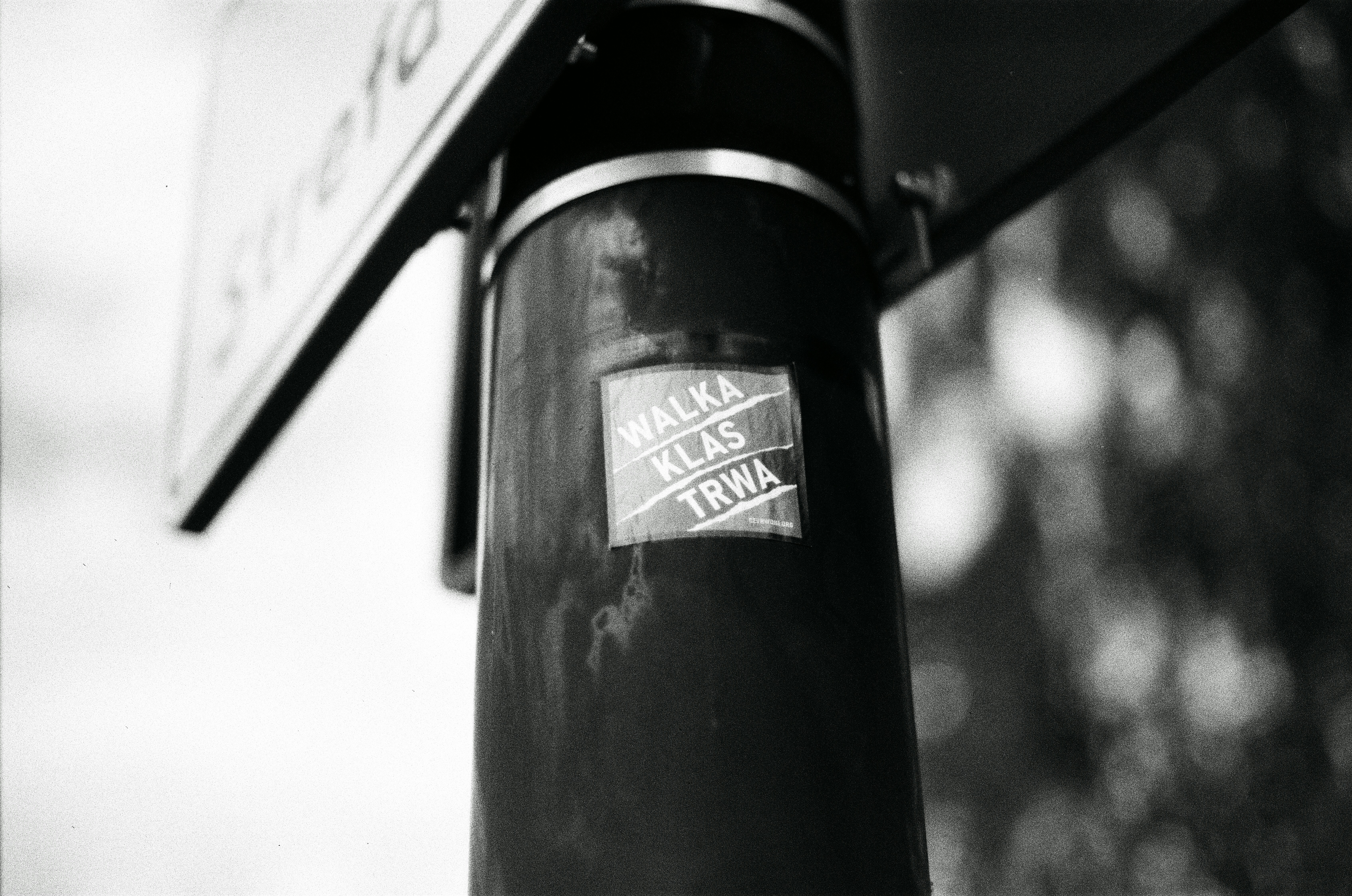Black and white close-up of a pole with a sticker.