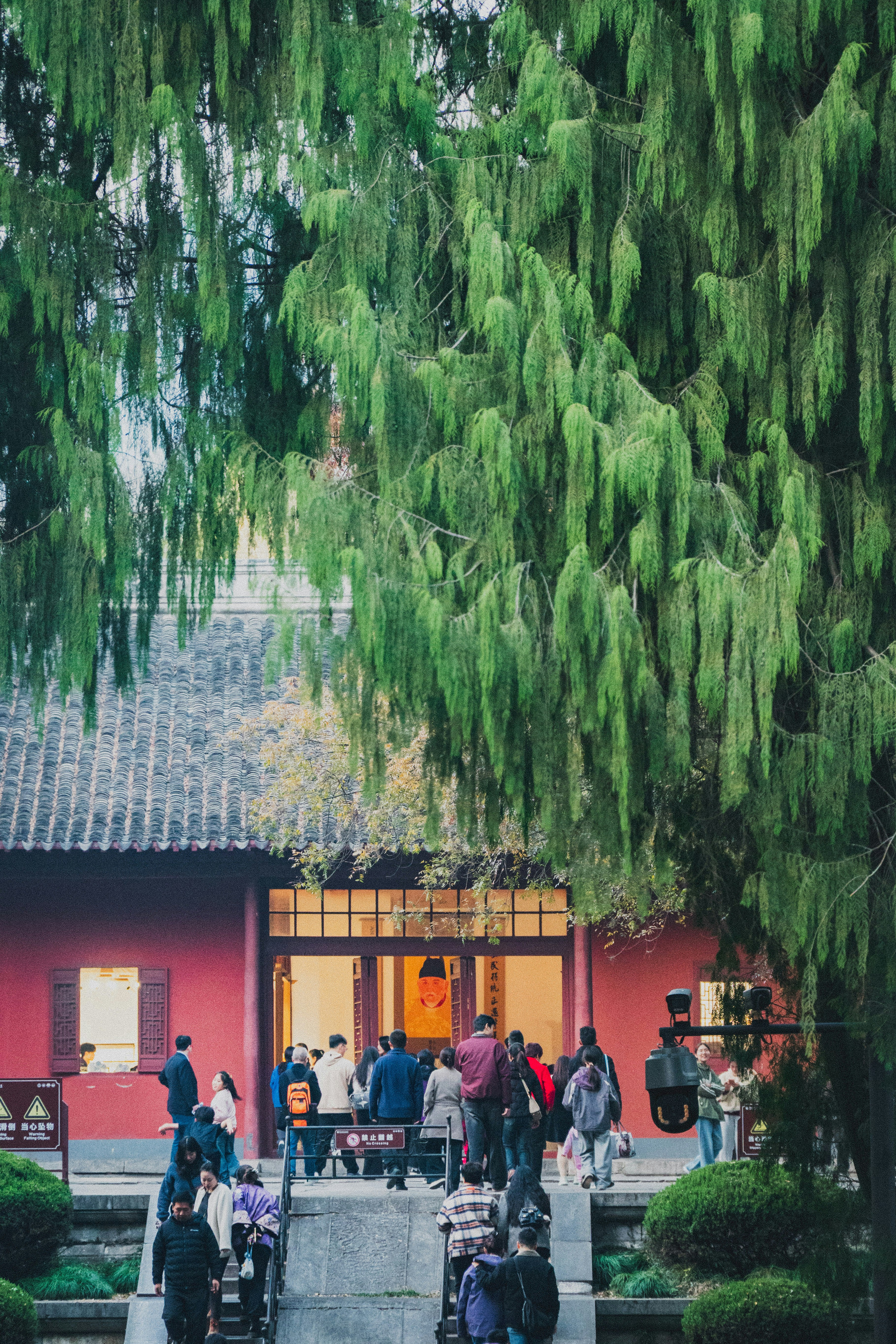People gather outside a red building under trees.