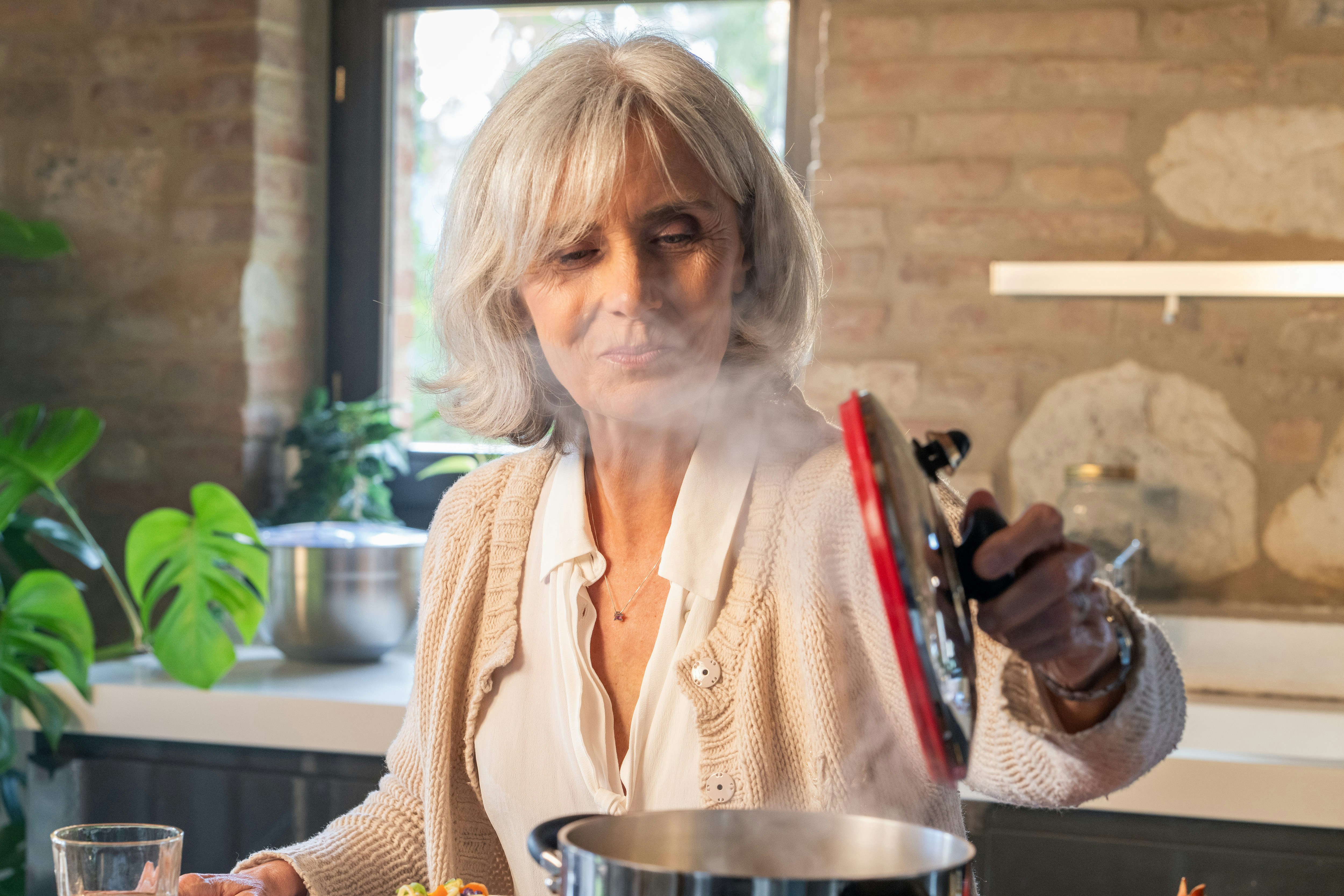 Eine ältere Frau hebt den Deckel vom dampfenden Topf