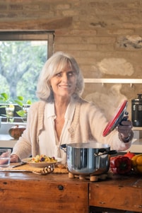 Smiling woman lifting lid from steaming pot of food