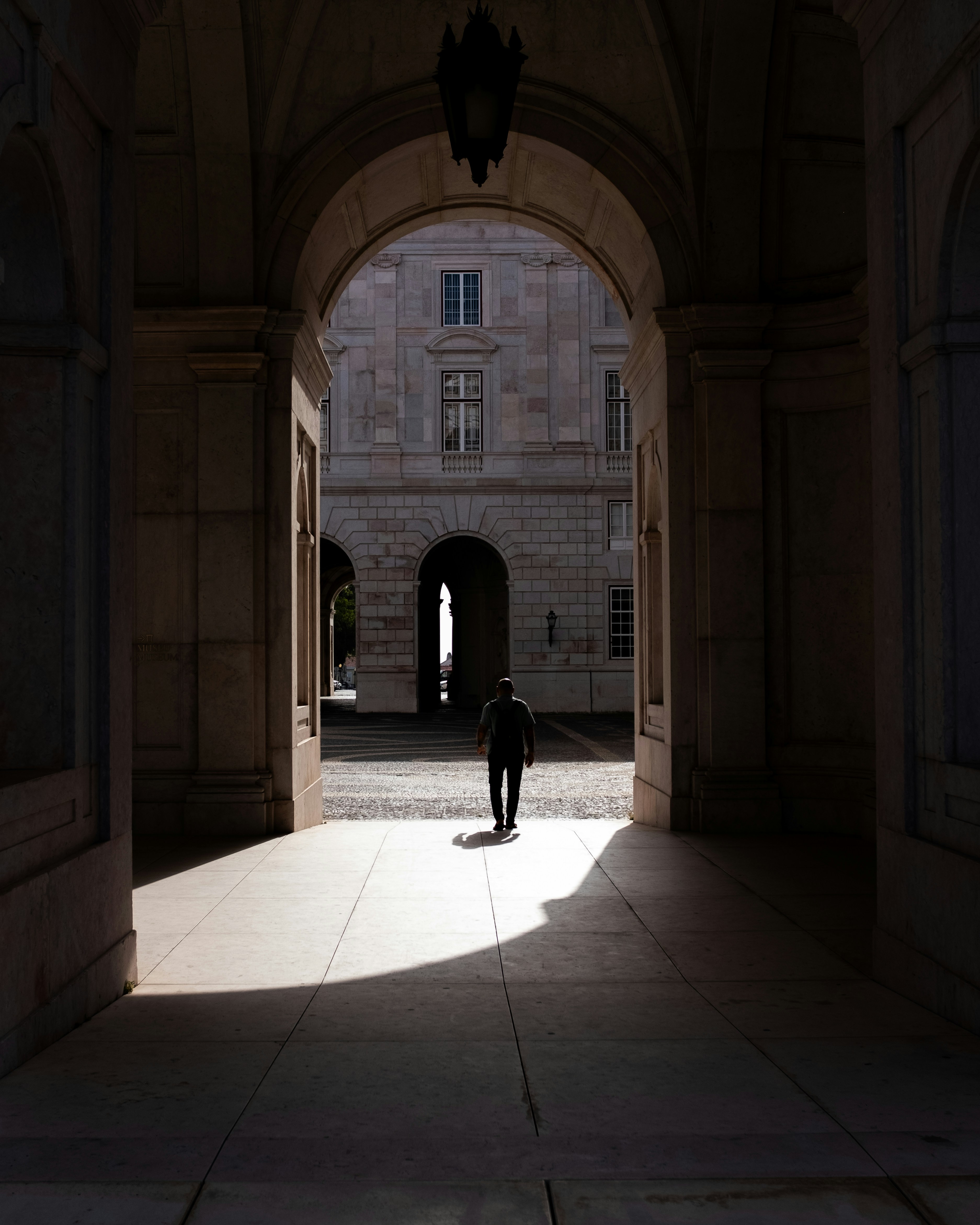 남자가 햇살이 비치는 아치형 입구를 지나 안뜰로 들어간다.