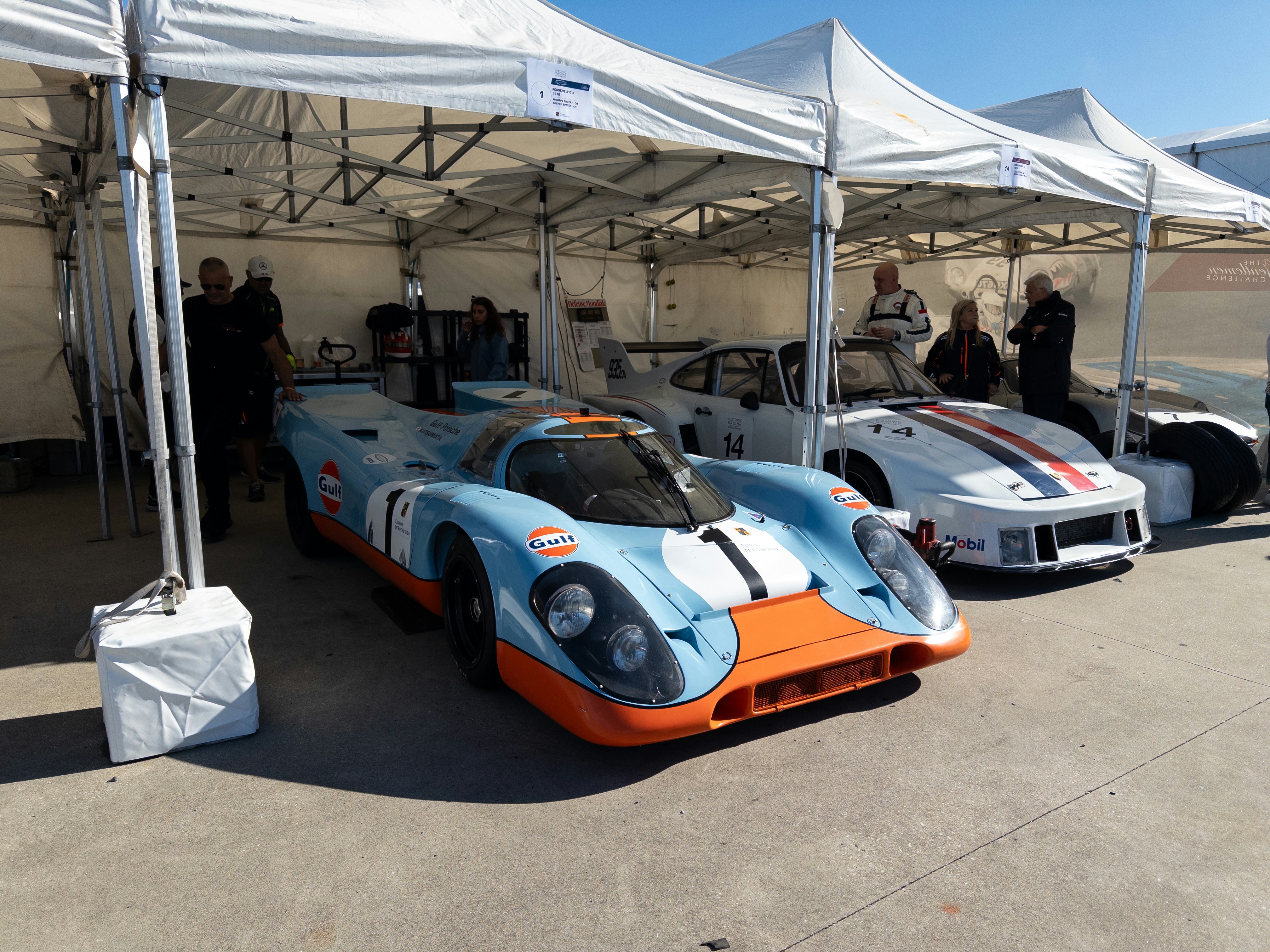 Two vintage race cars parked under tents.