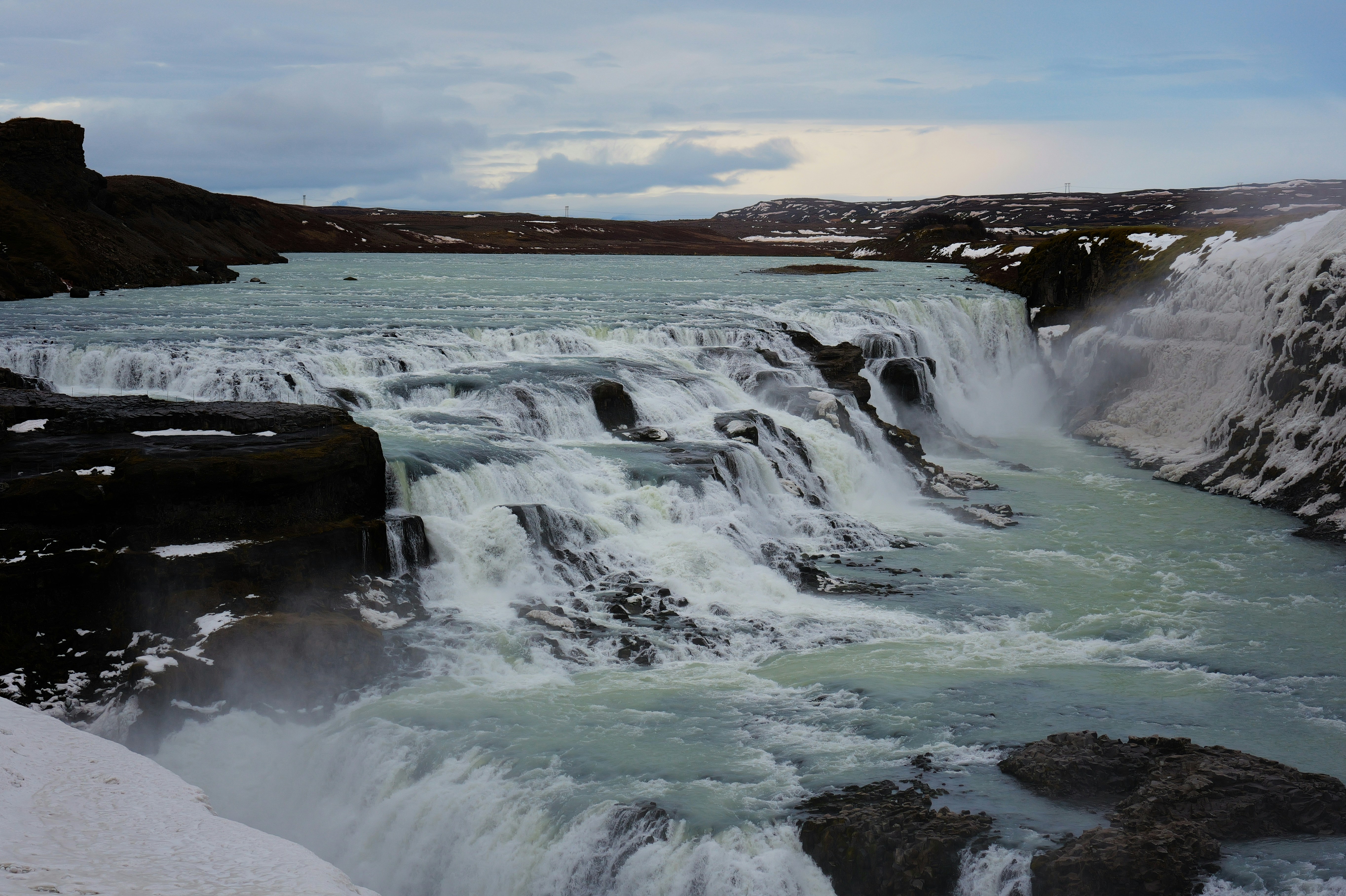 A wide waterfall cascades over rocks in a snowy landscape.