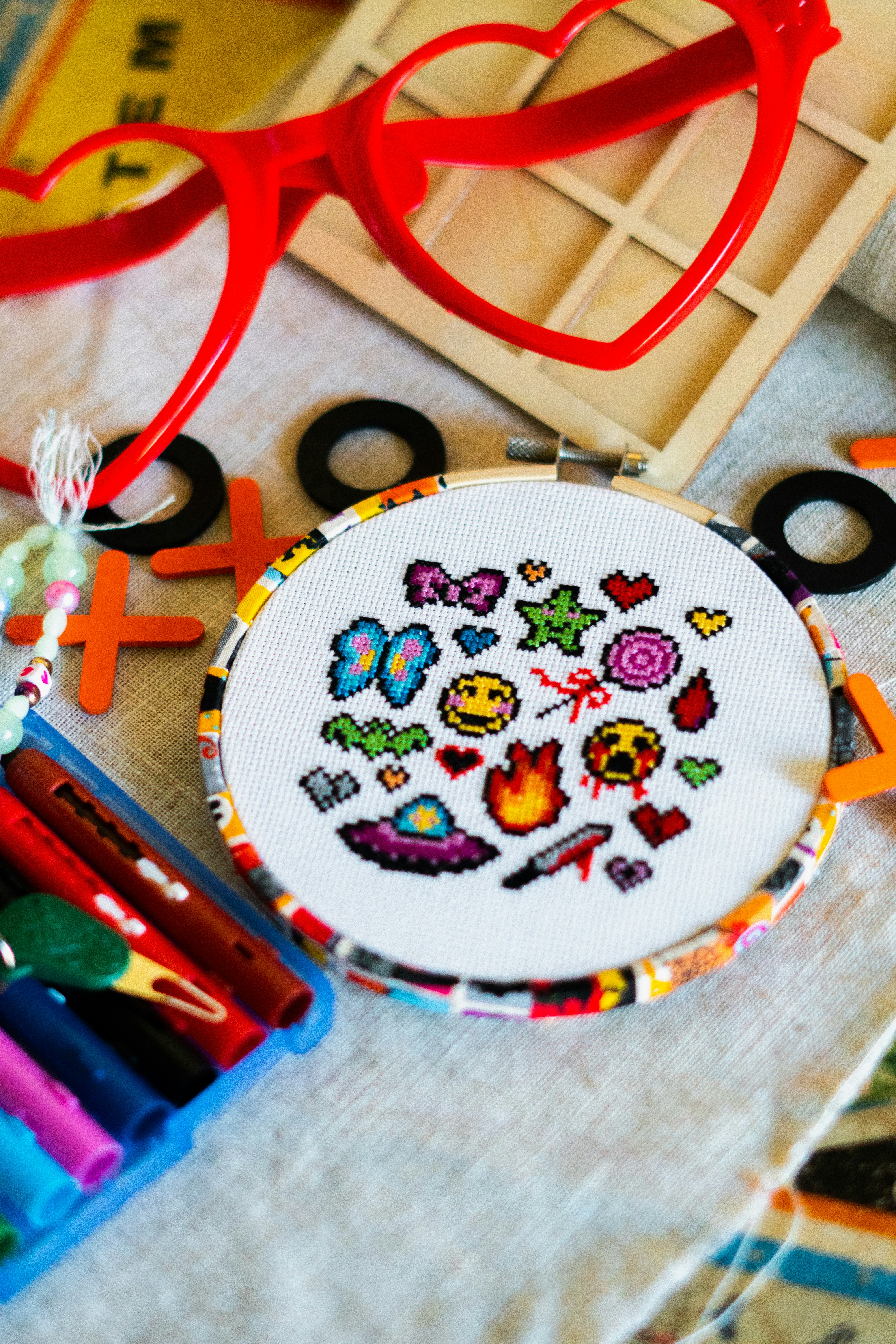 Cross-stitch hoop with colorful pixelated icons and craft supplies.