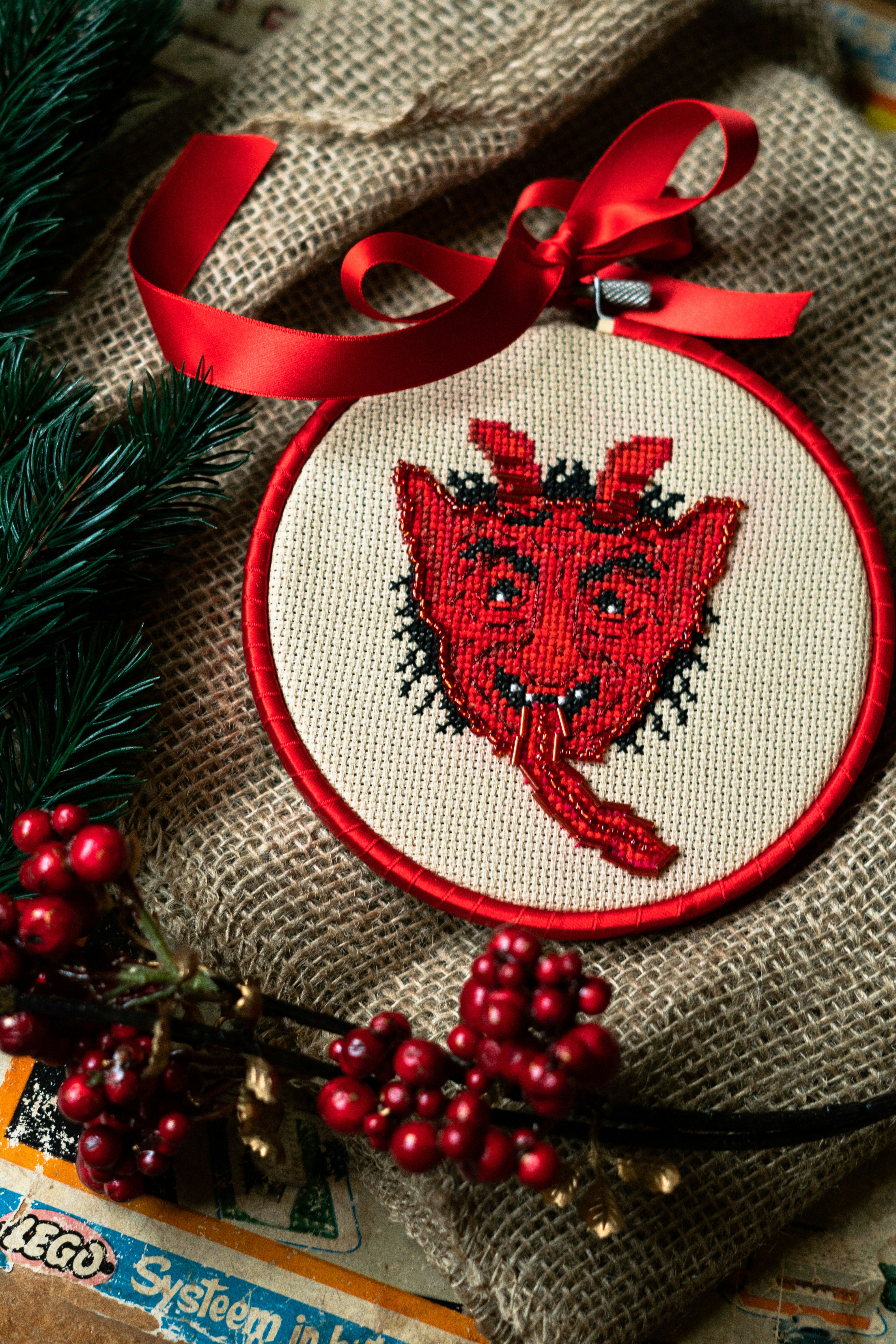 Red devil cross-stitch ornament with ribbon and berries