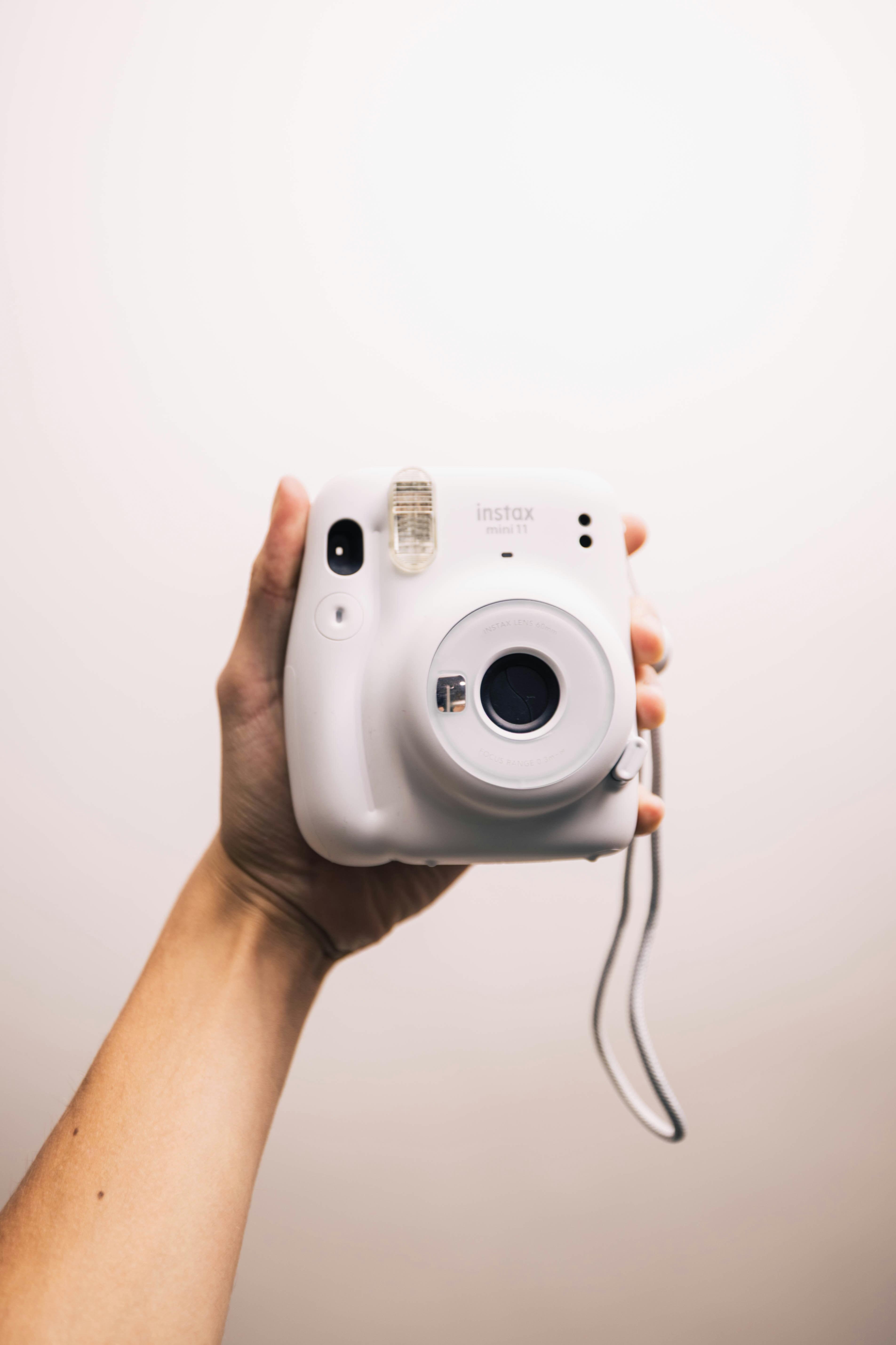 Hand holding a white instant camera against a white background