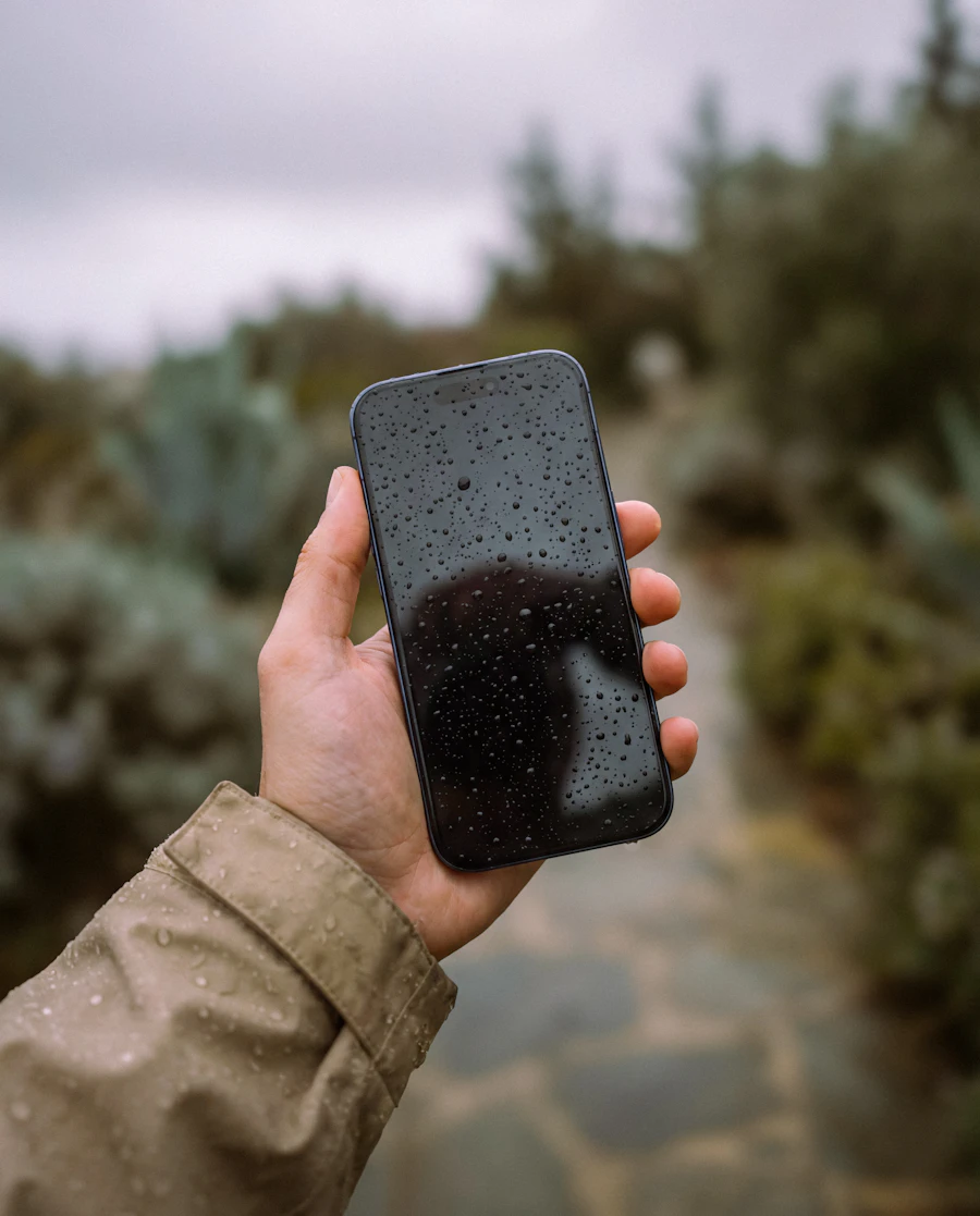 Hand holding a wet smartphone outdoors with water droplets visible on the screen