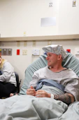 Man in hospital gown wearing surgical cap smiles.