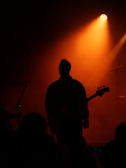 Silhouette of a guitarist on stage with orange spotlight.