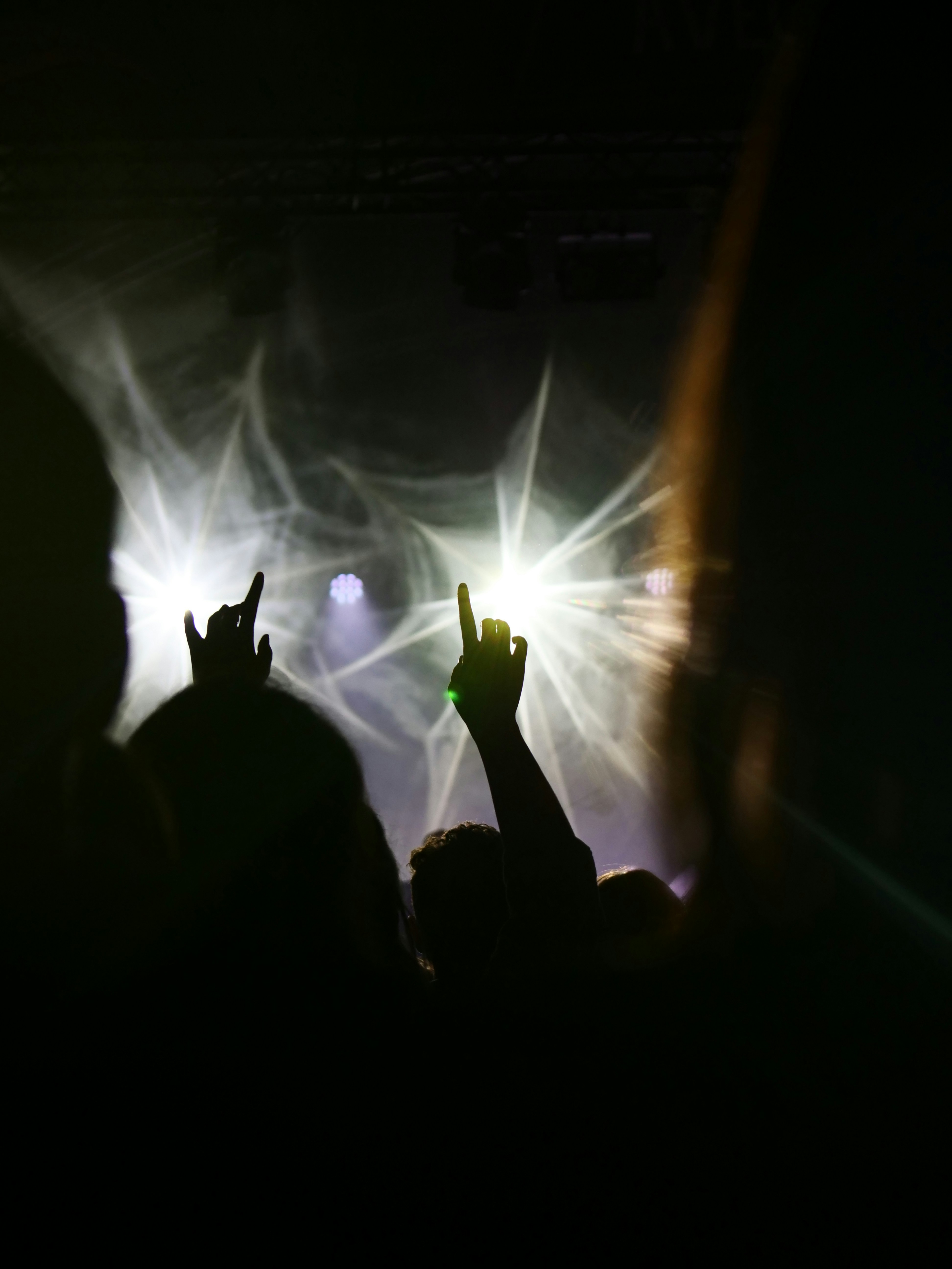 Hands raised at a concert with bright lights.