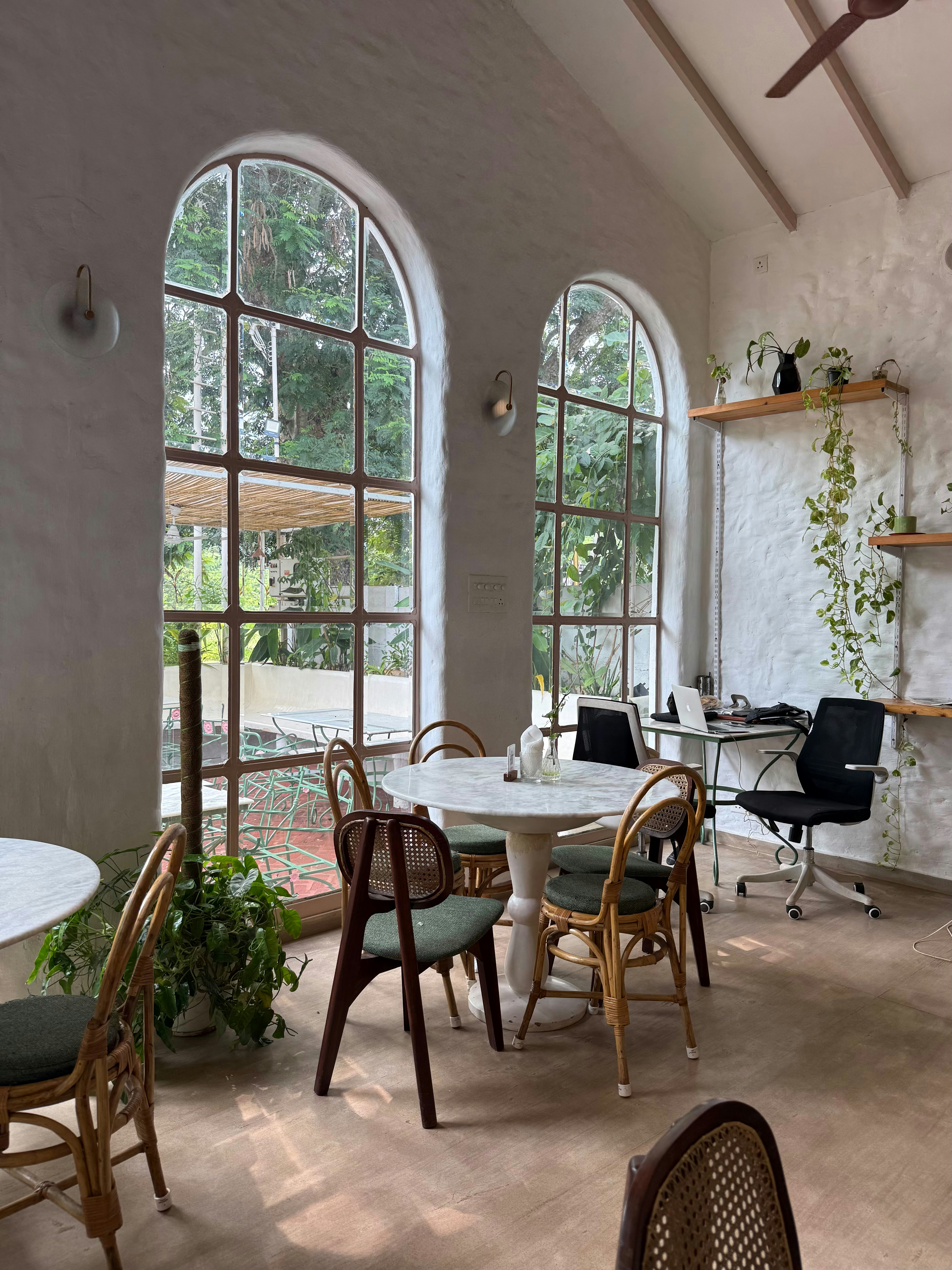 Light-filled café with arched windows, marble tables, rattan chairs and planting