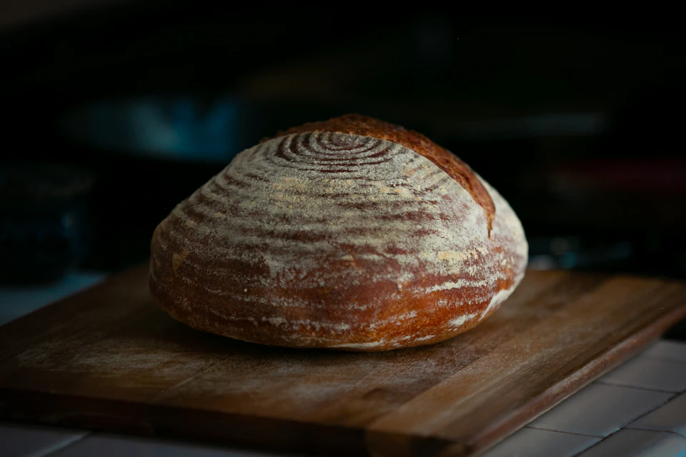 Freshly baked golden brown crust loaf of bread on wooden cutting board countertop