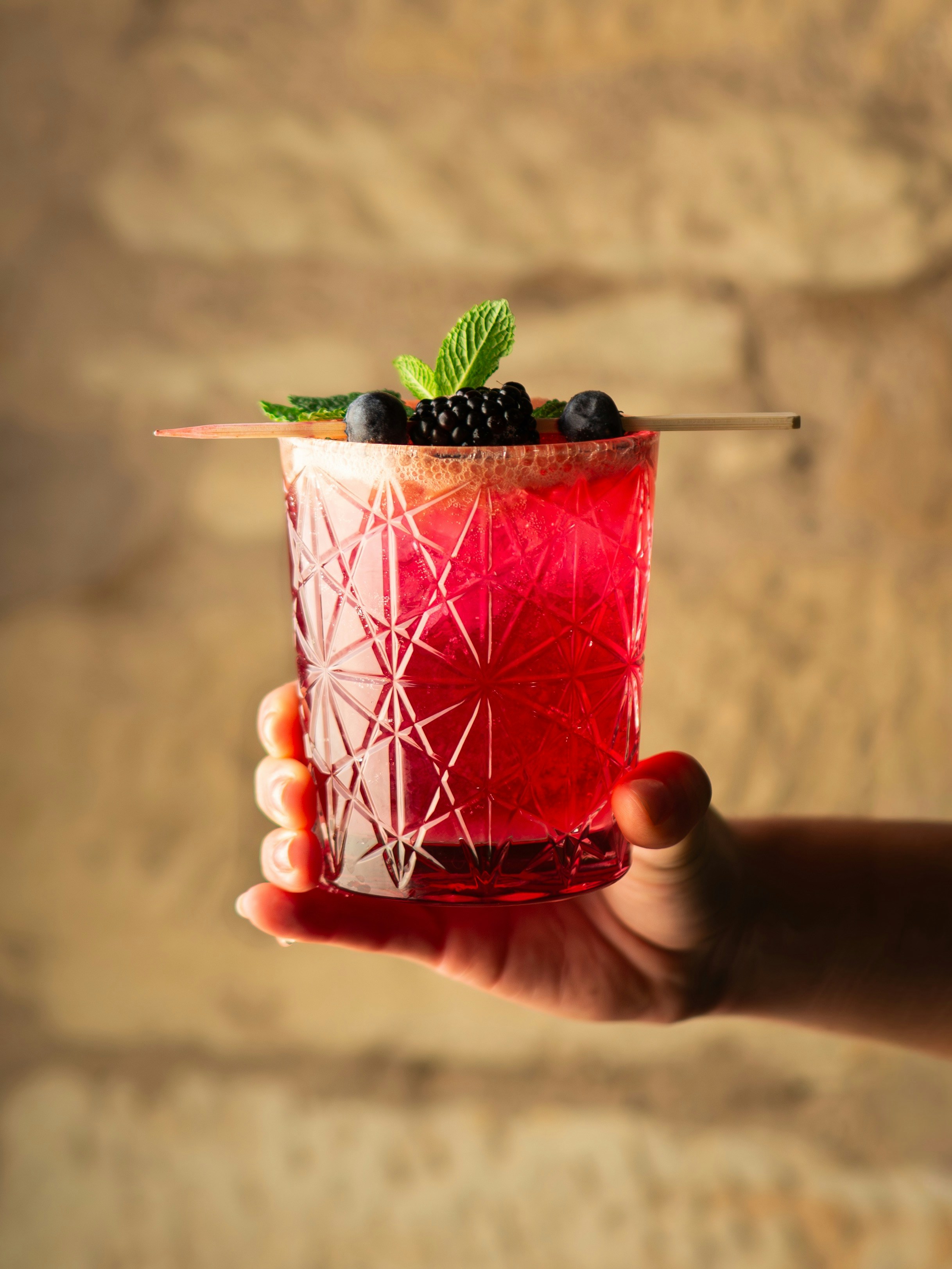 Sosteniendo de la mano un cóctel de frutos rojos vibrantes con adorno de menta.
