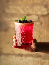 Hand holding a vibrant berry cocktail with mint garnish.