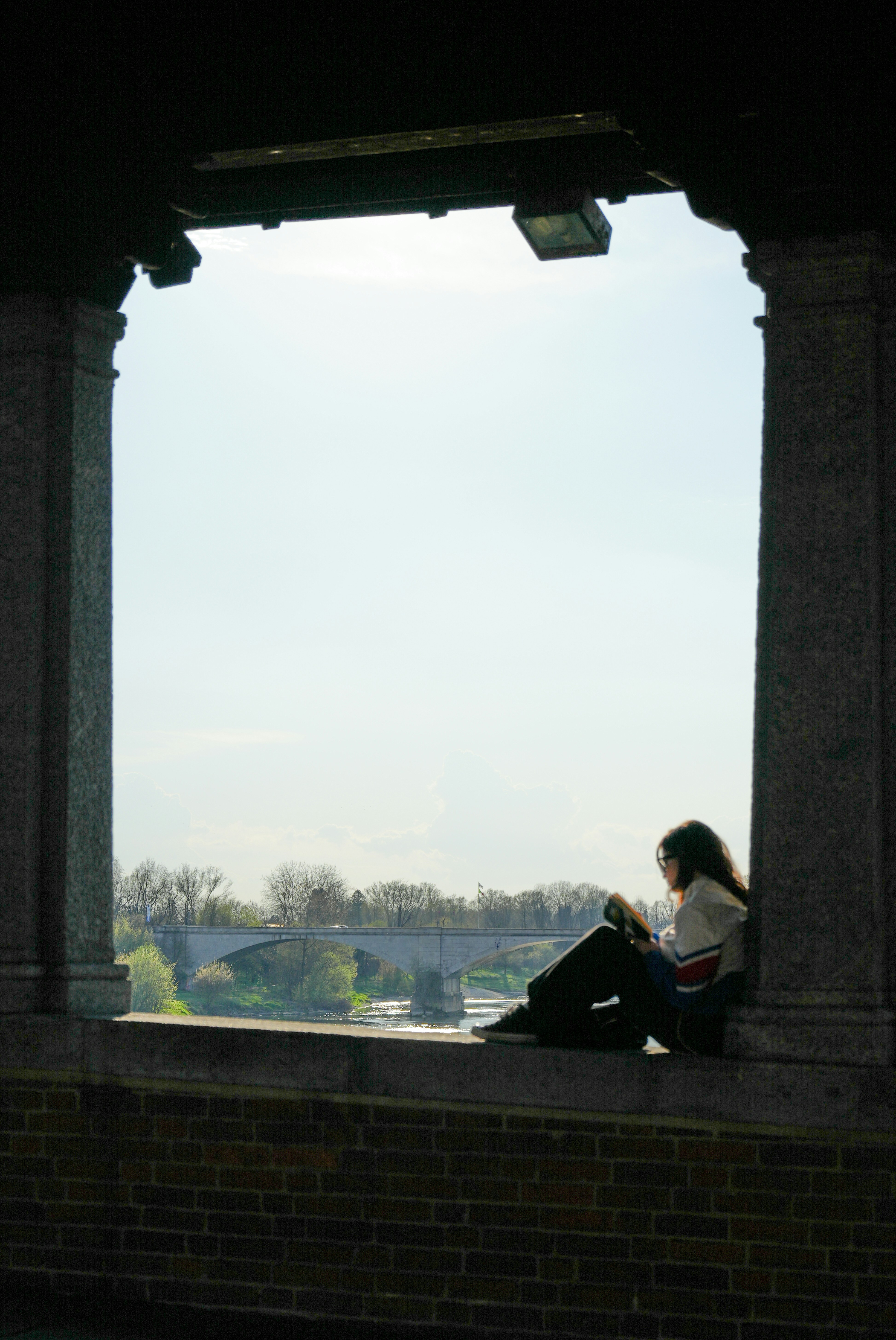 Woman sitting and looking at phone through stone archway