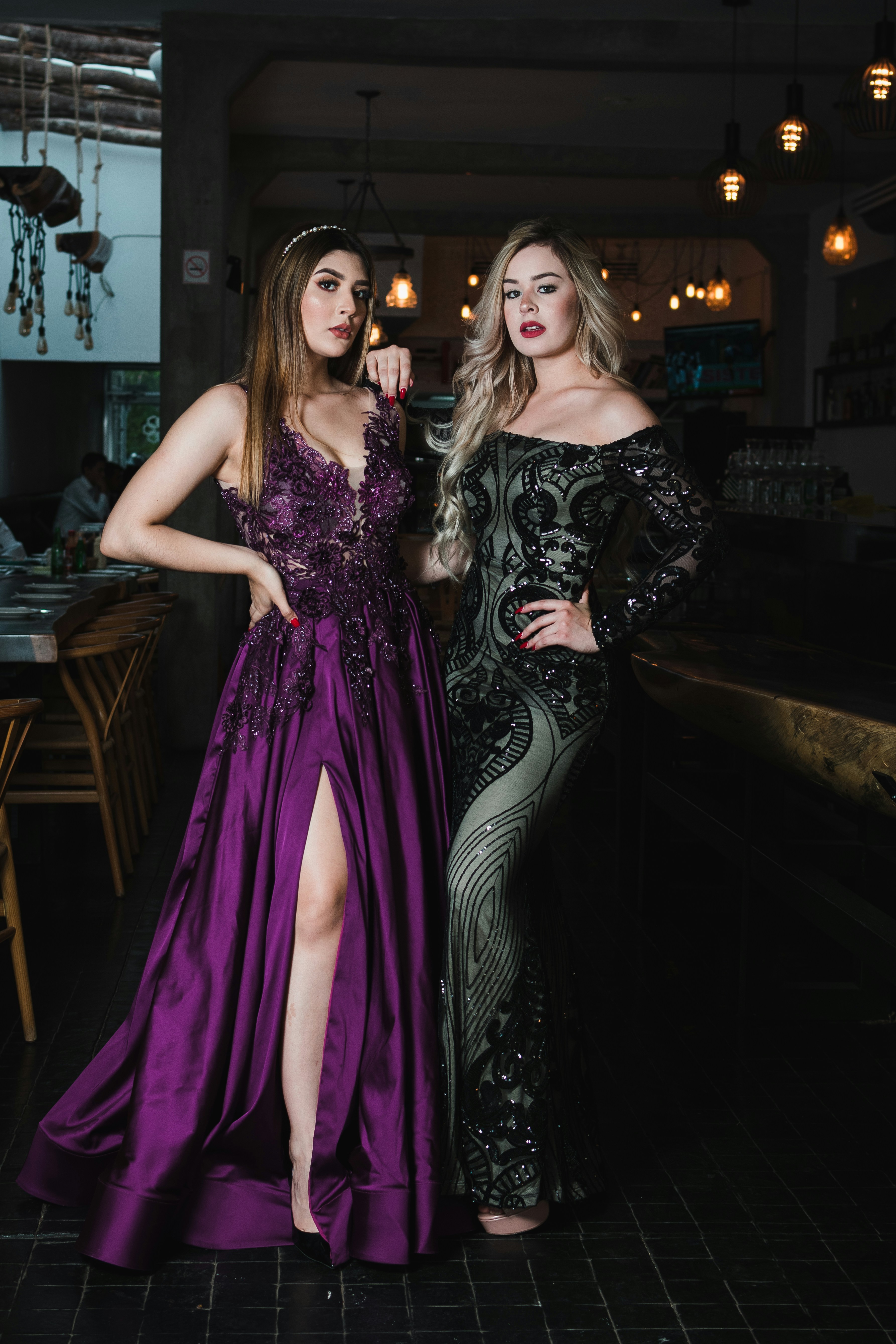 Two women in elegant gowns posing indoors.
