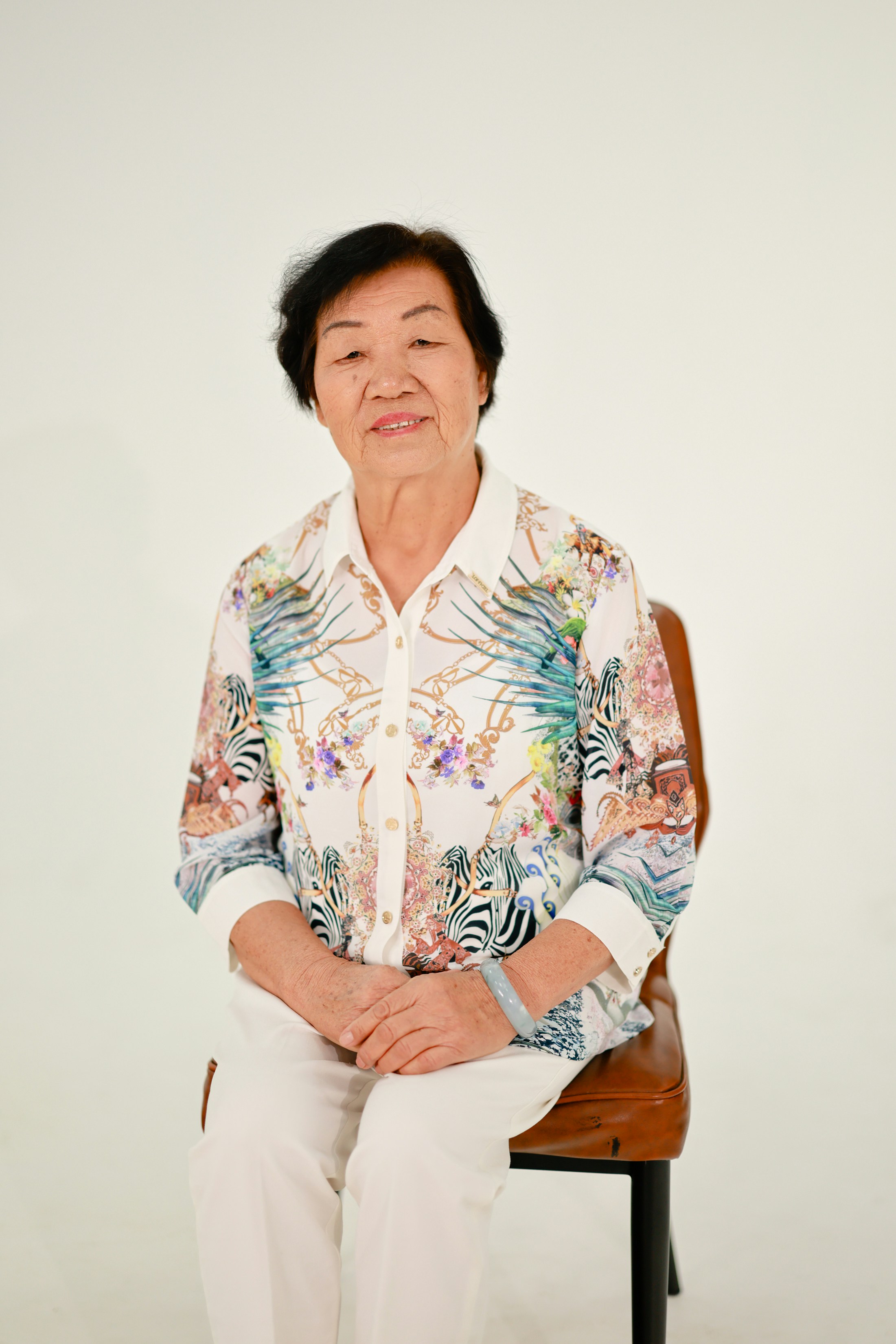 Uma senhora asiática idosa está sentada em uma cadeira.