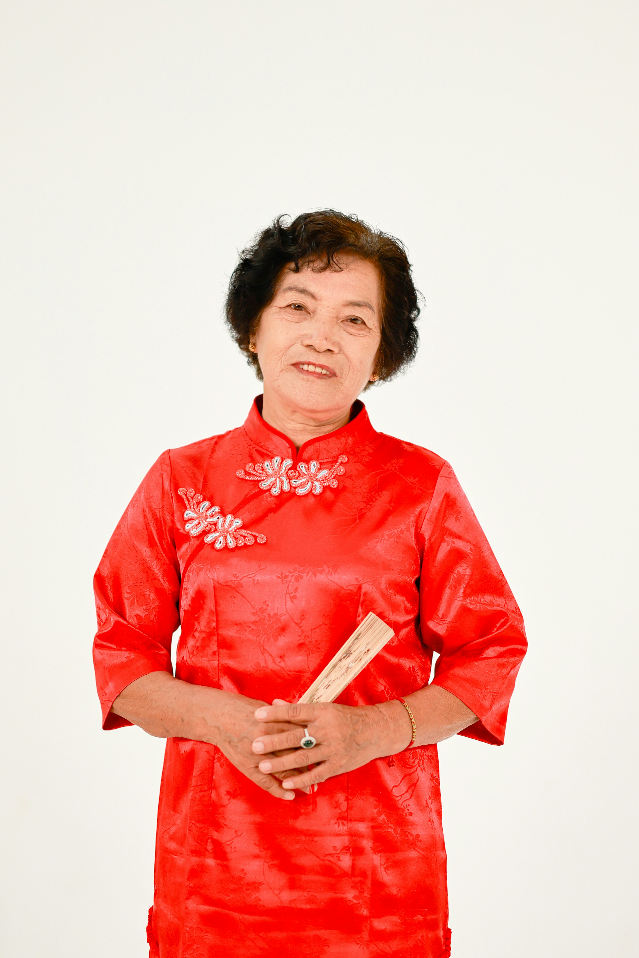 Elderly asian woman in red dress holding a fan.