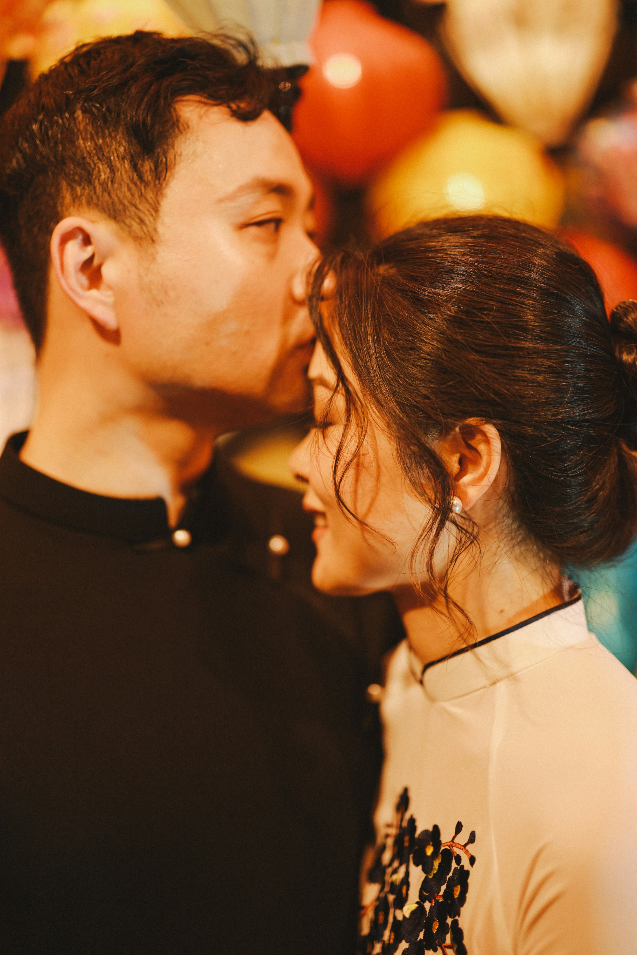 Man kissing woman's forehead with colorful balloons