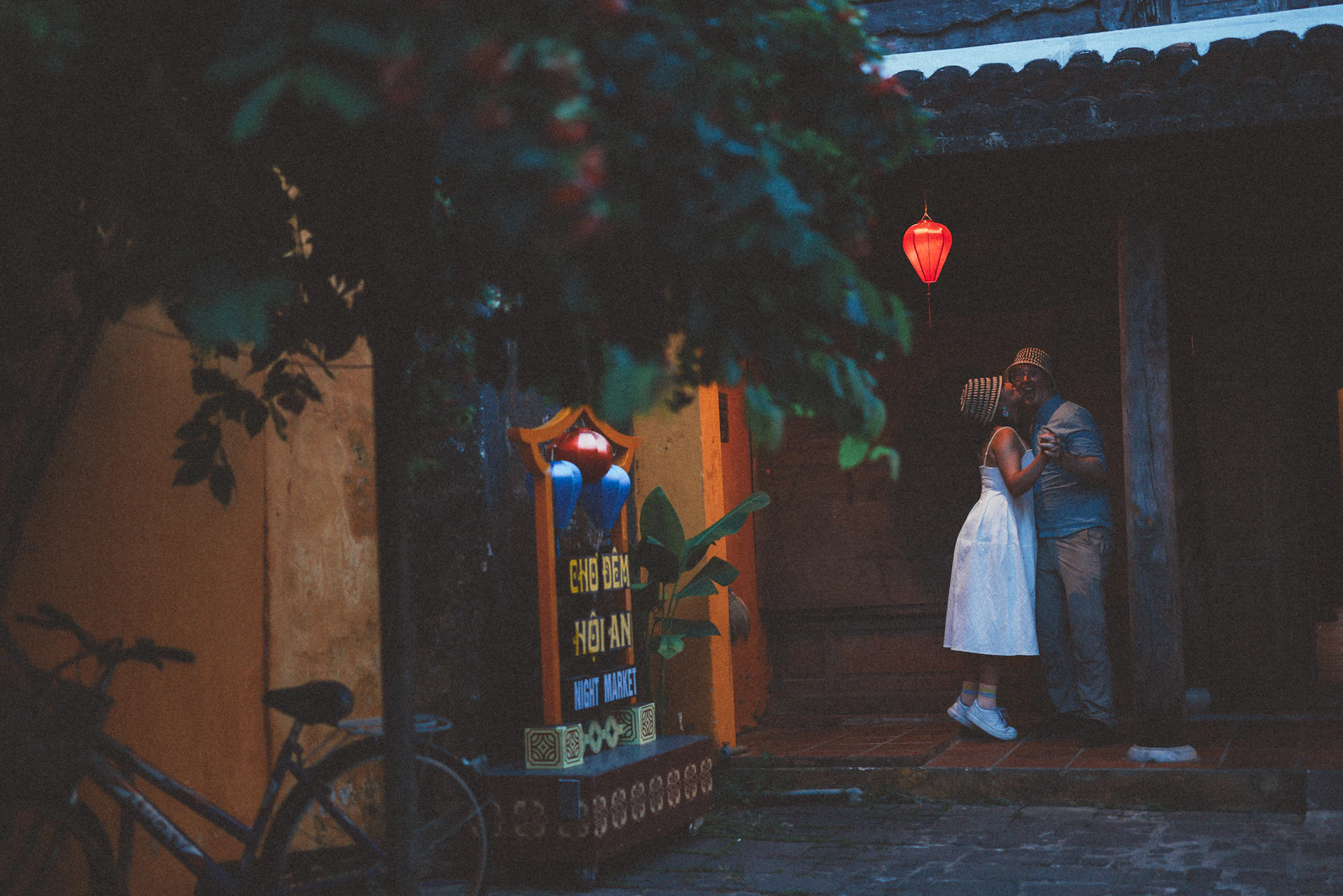 Couple embracing under a red lantern at dusk.