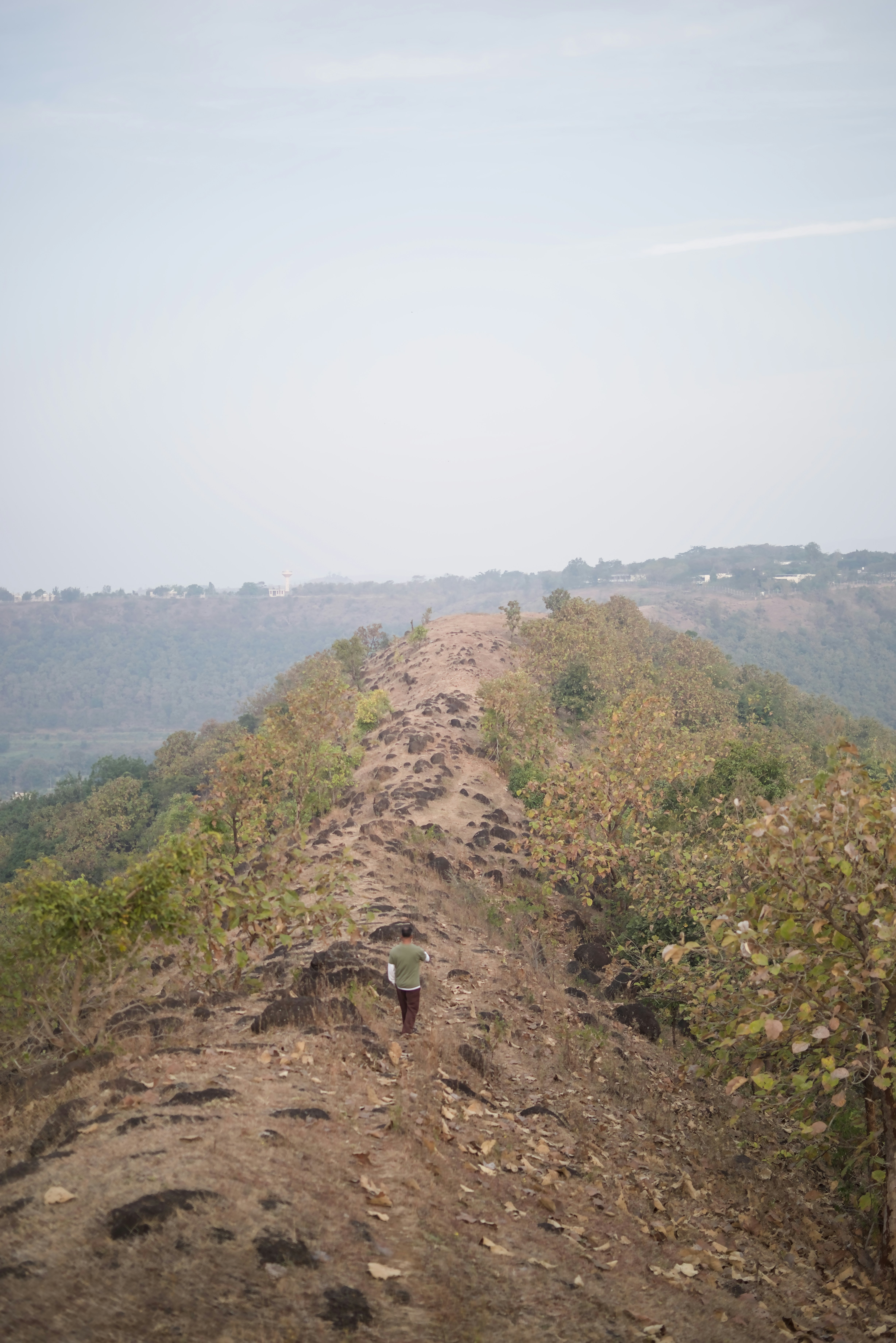A person walks on a narrow mountain ridge path.
