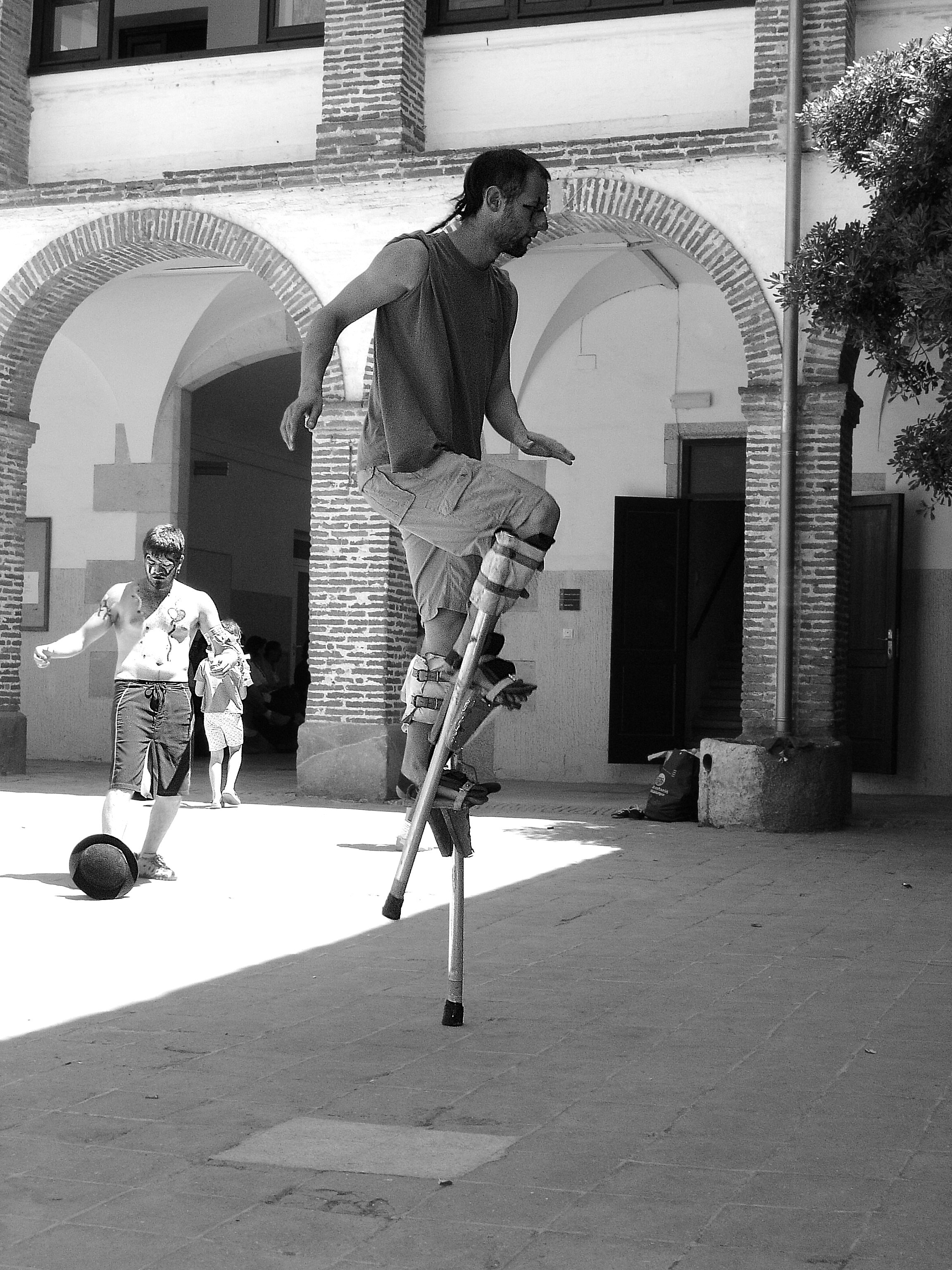 Man on stilts in courtyard with children playing.