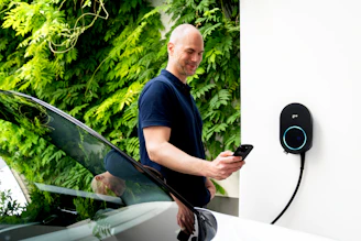 Man using phone near electric car charging station.