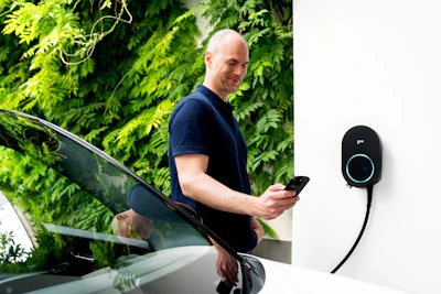 Man using phone near electric car charging station.