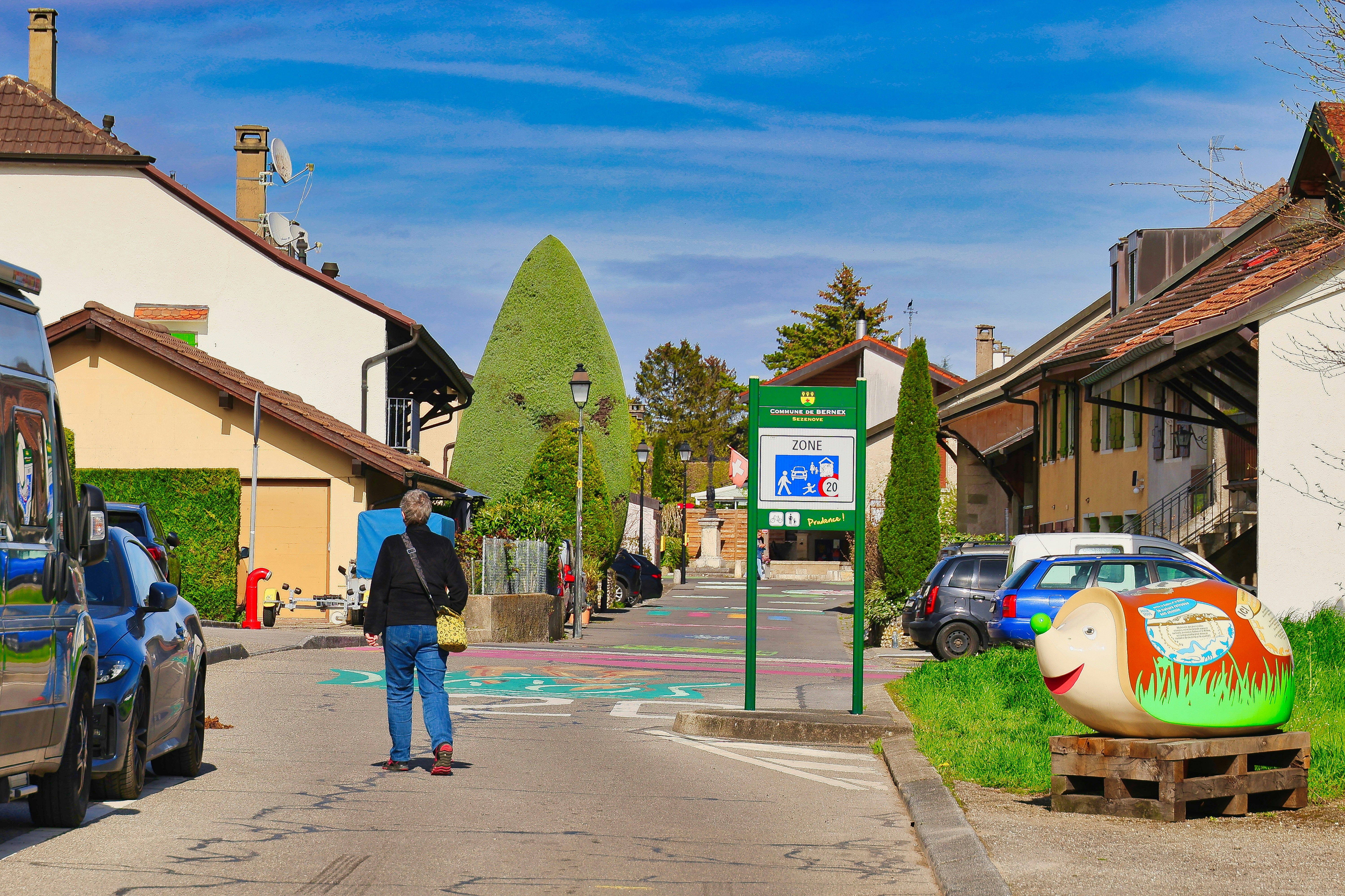 A man stands on a street with houses and cars.
