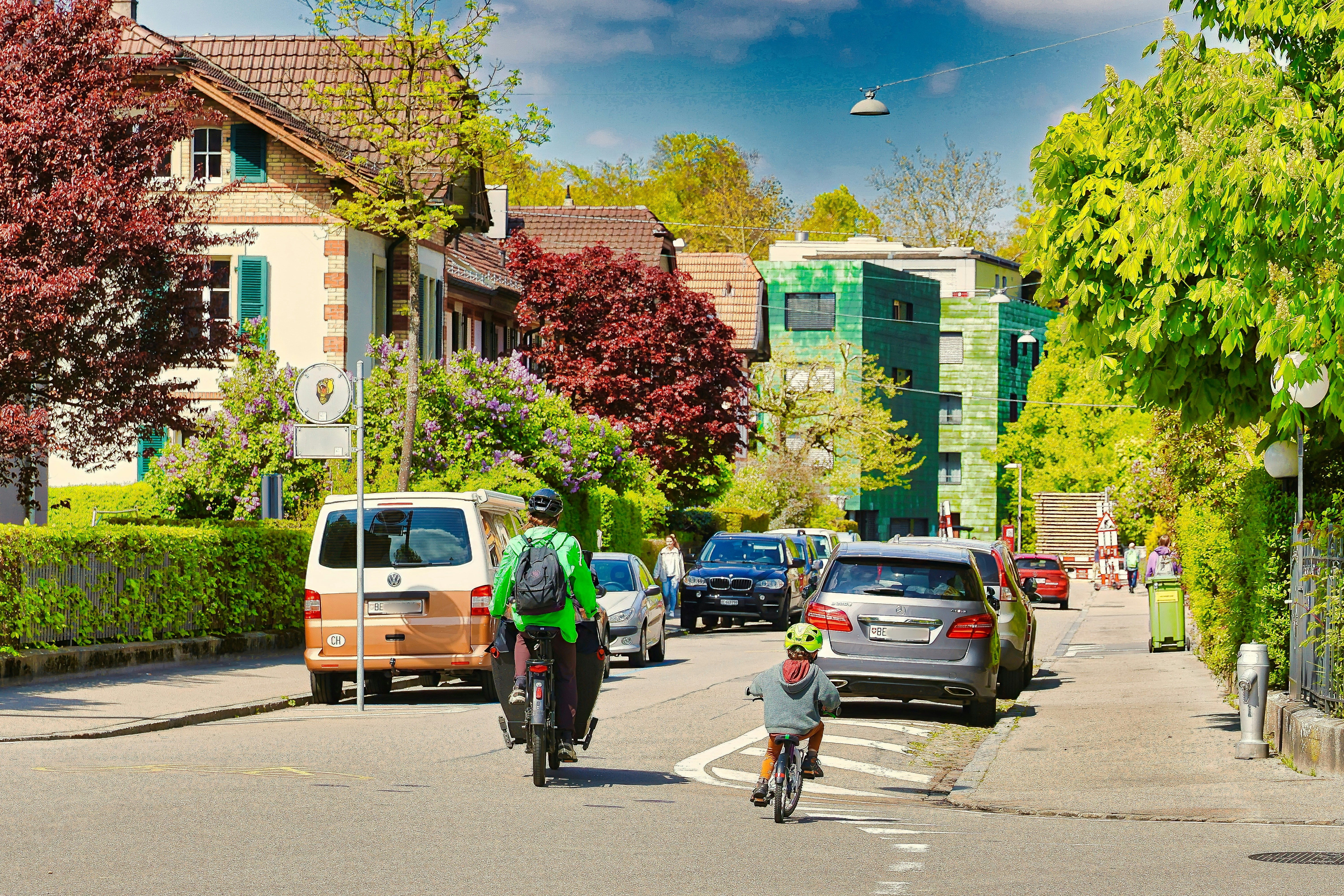People cycling on a street with cars and houses.