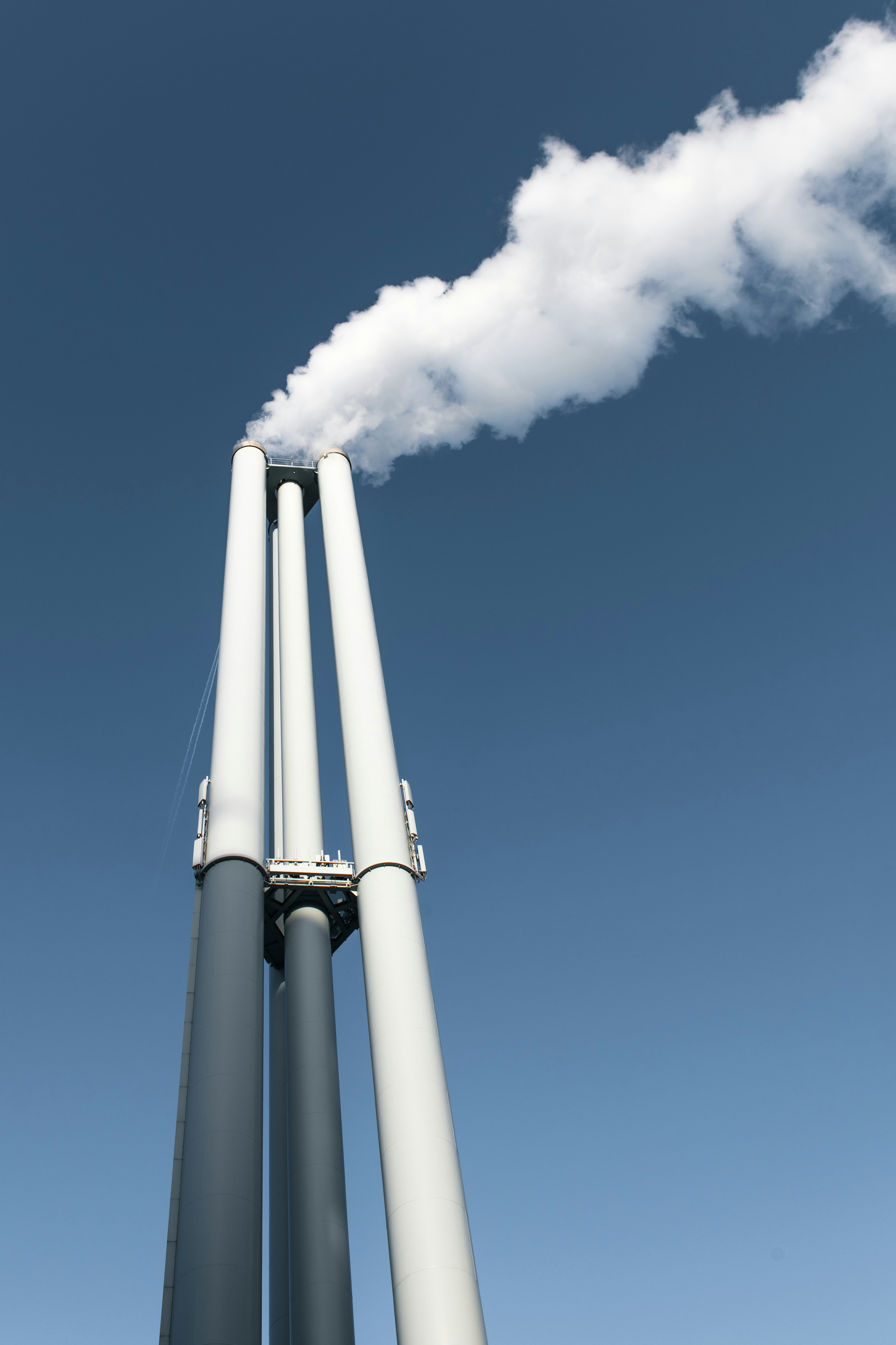 Three smokestacks emitting white smoke against blue sky